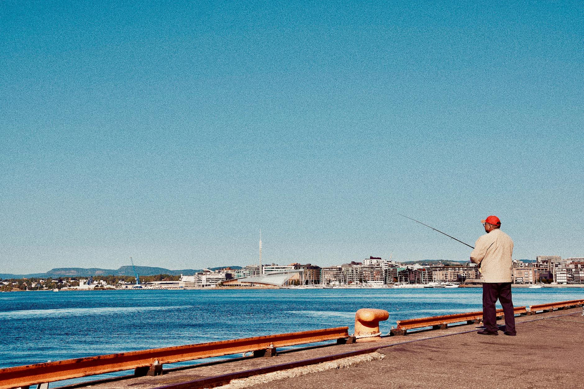 Person fishing on a pier with Oslo cityscape behind