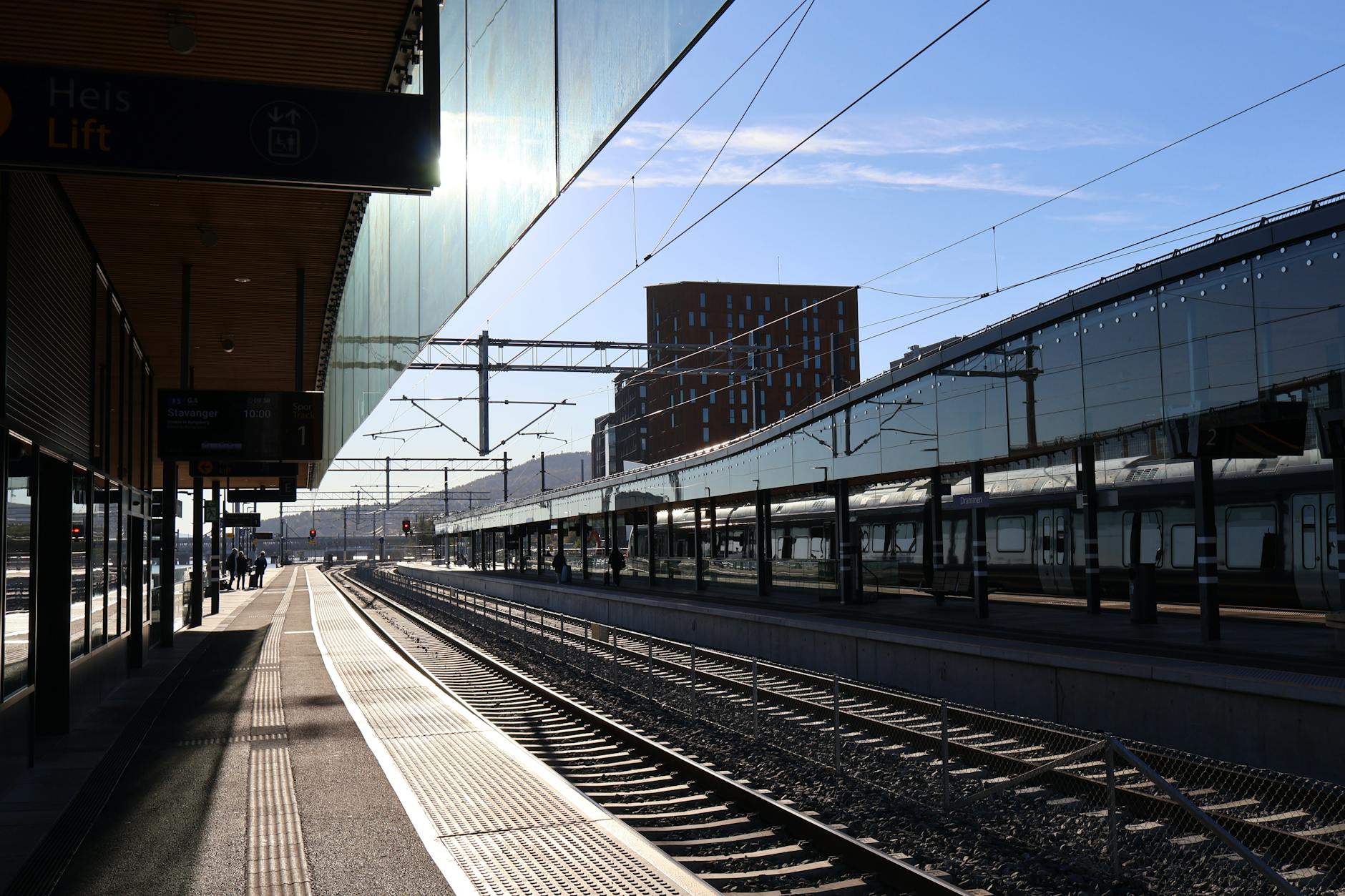 Sunlit Norwegian train station with empty tracks and modern architecture