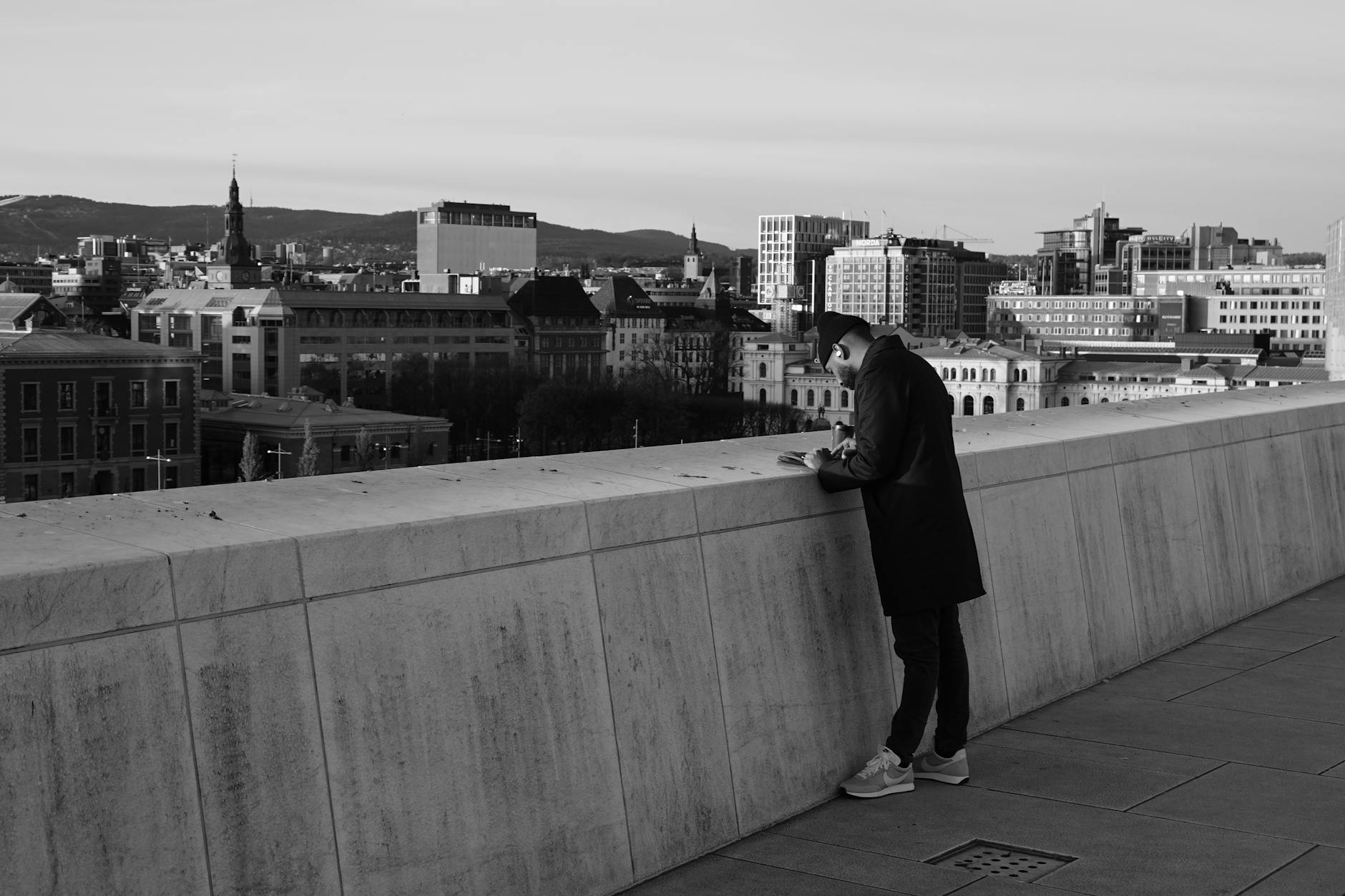 Person leaning on the Oslo Opera House rooftop overlooking the city