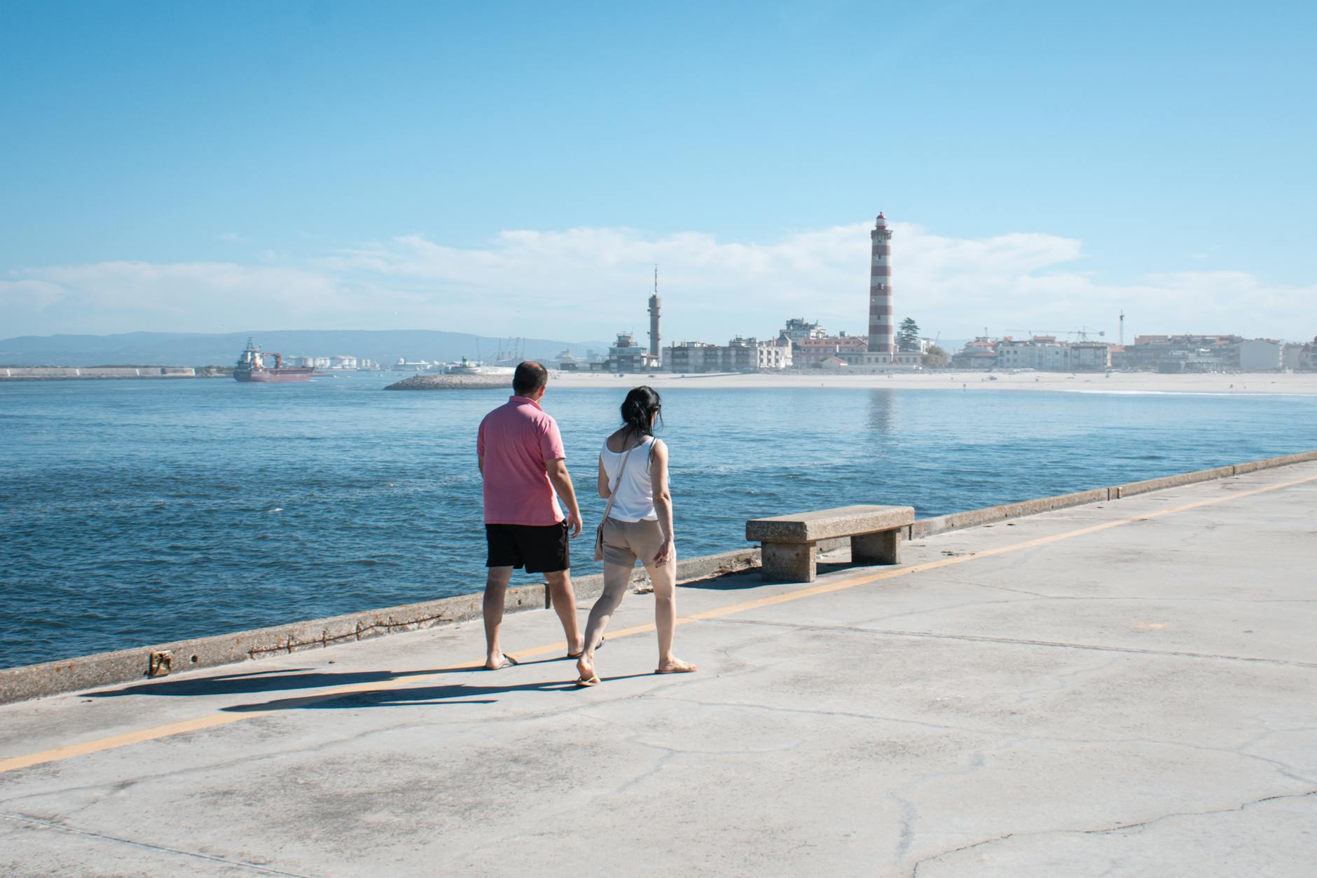 Couple walking along the waterfront near a distant lighthouse