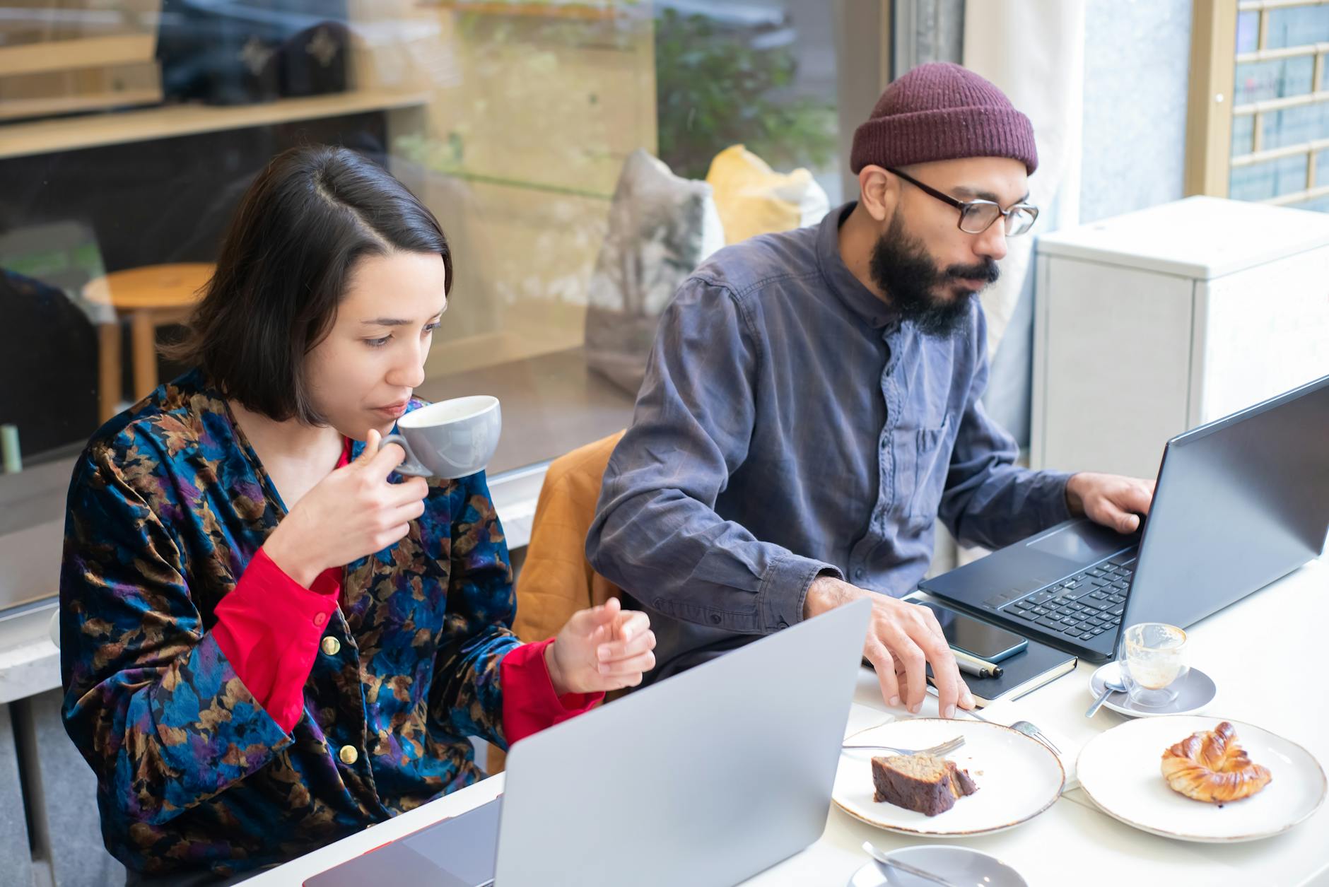 Two adults working on laptops in a contemporary cafe