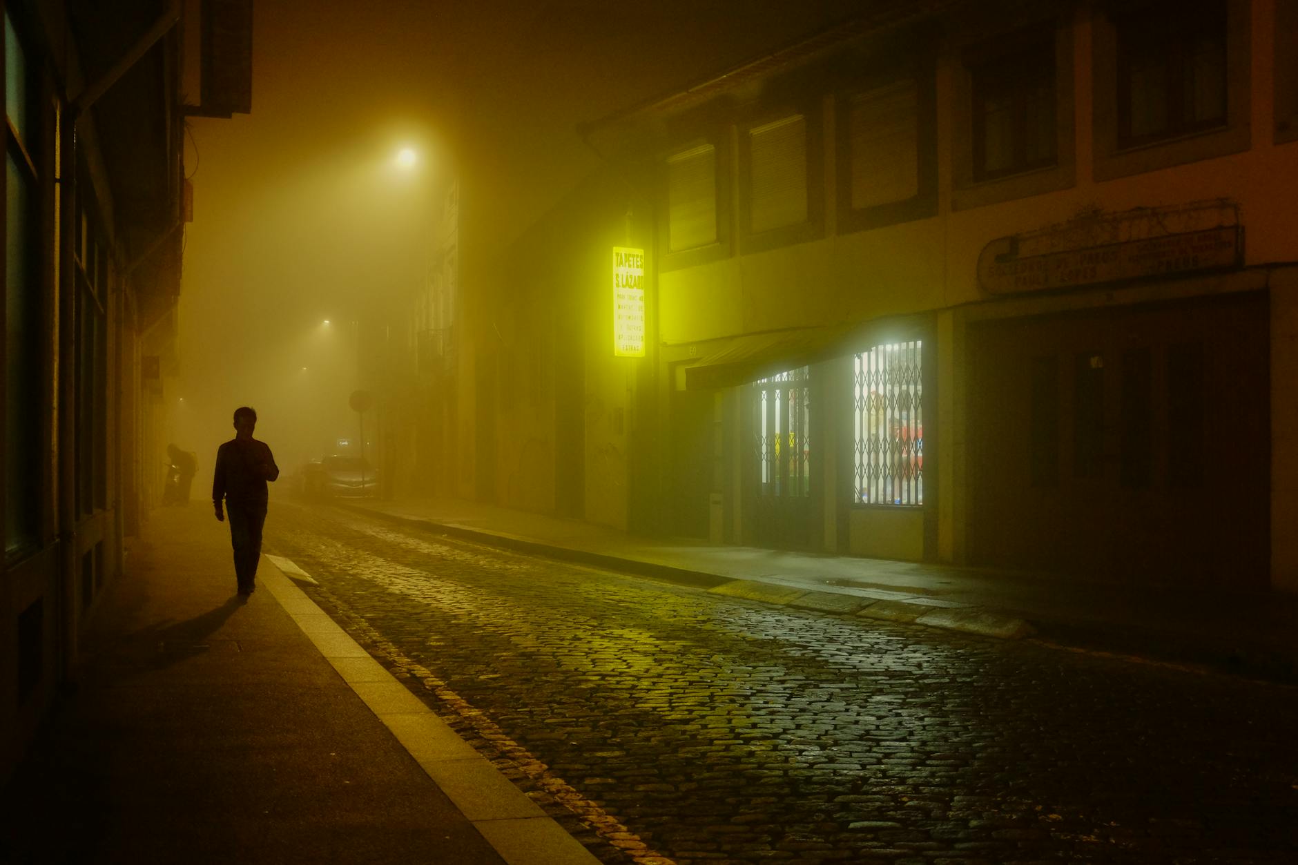 Lone figure walking through a foggy illuminated Porto street at night