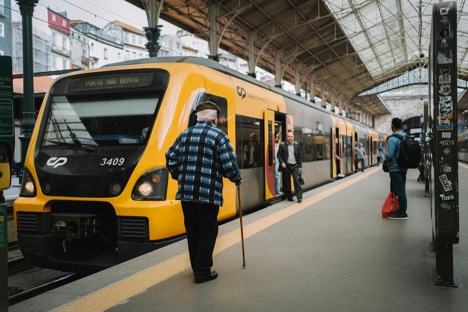 Senior man with walking stick beside a yellow train at Porto Sao Bento station