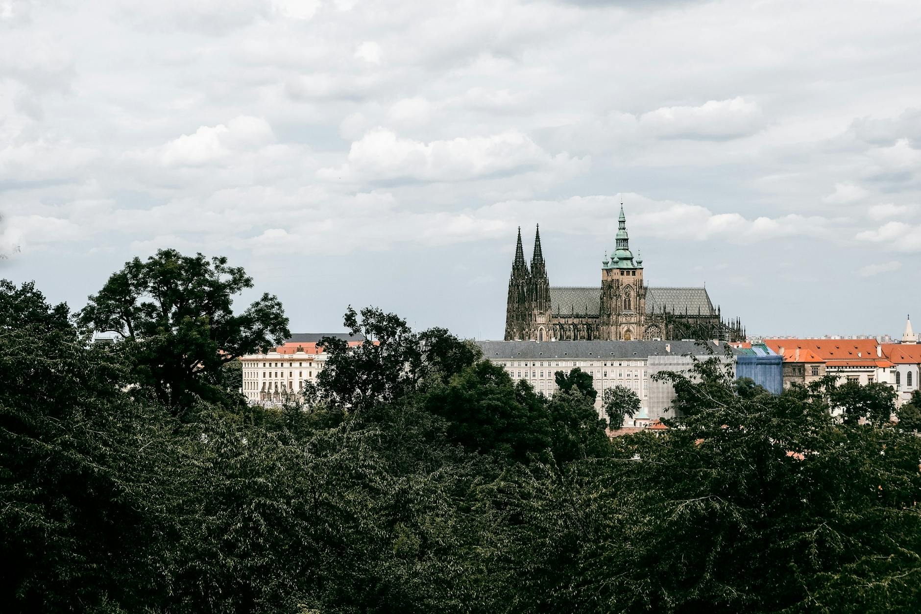 Prague Castle viewed above lush greenery under cloudy sky