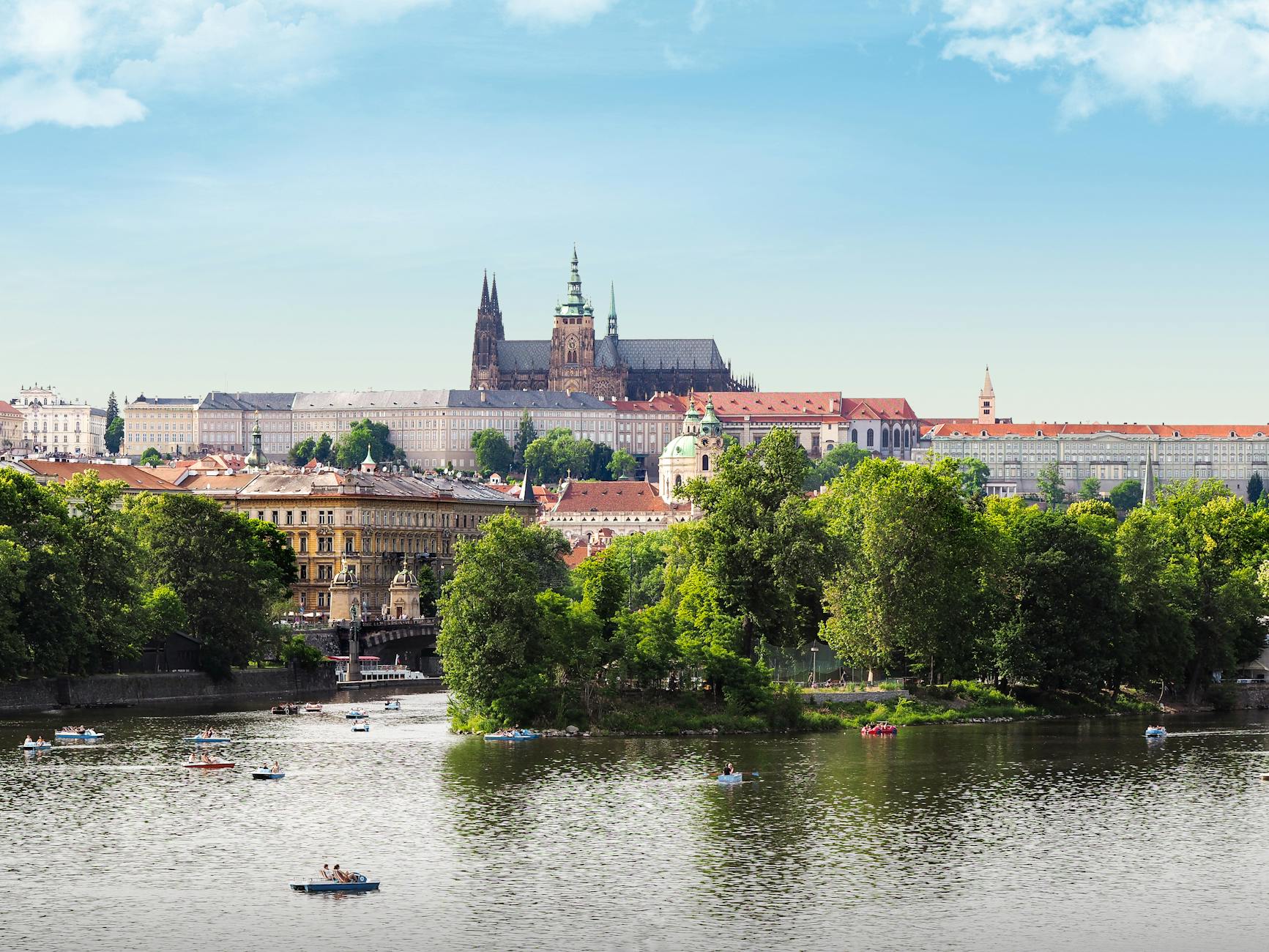 Prague Castle, Vltava River, boats, and trees on a sunny day