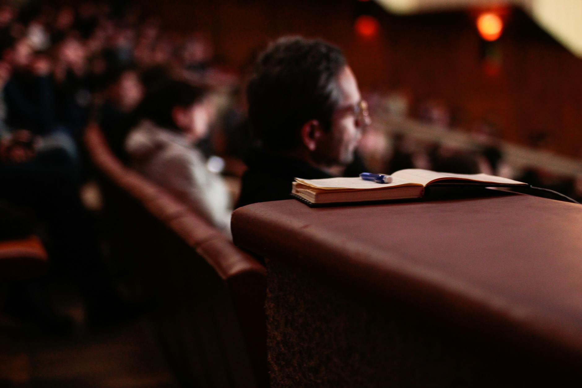 Notebook and pen in an auditorium with audience in the background