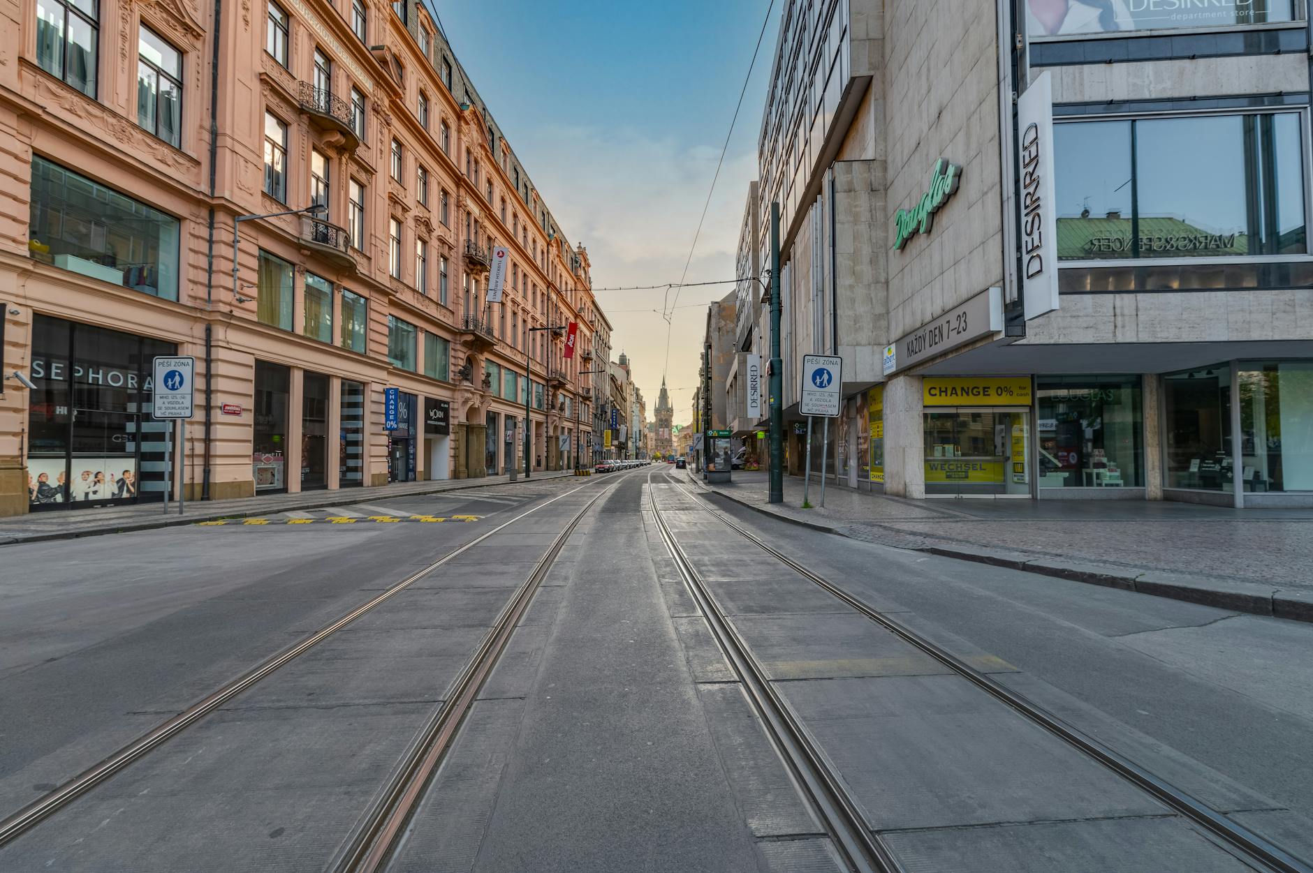Prague street with shops and tramway tracks at sunset