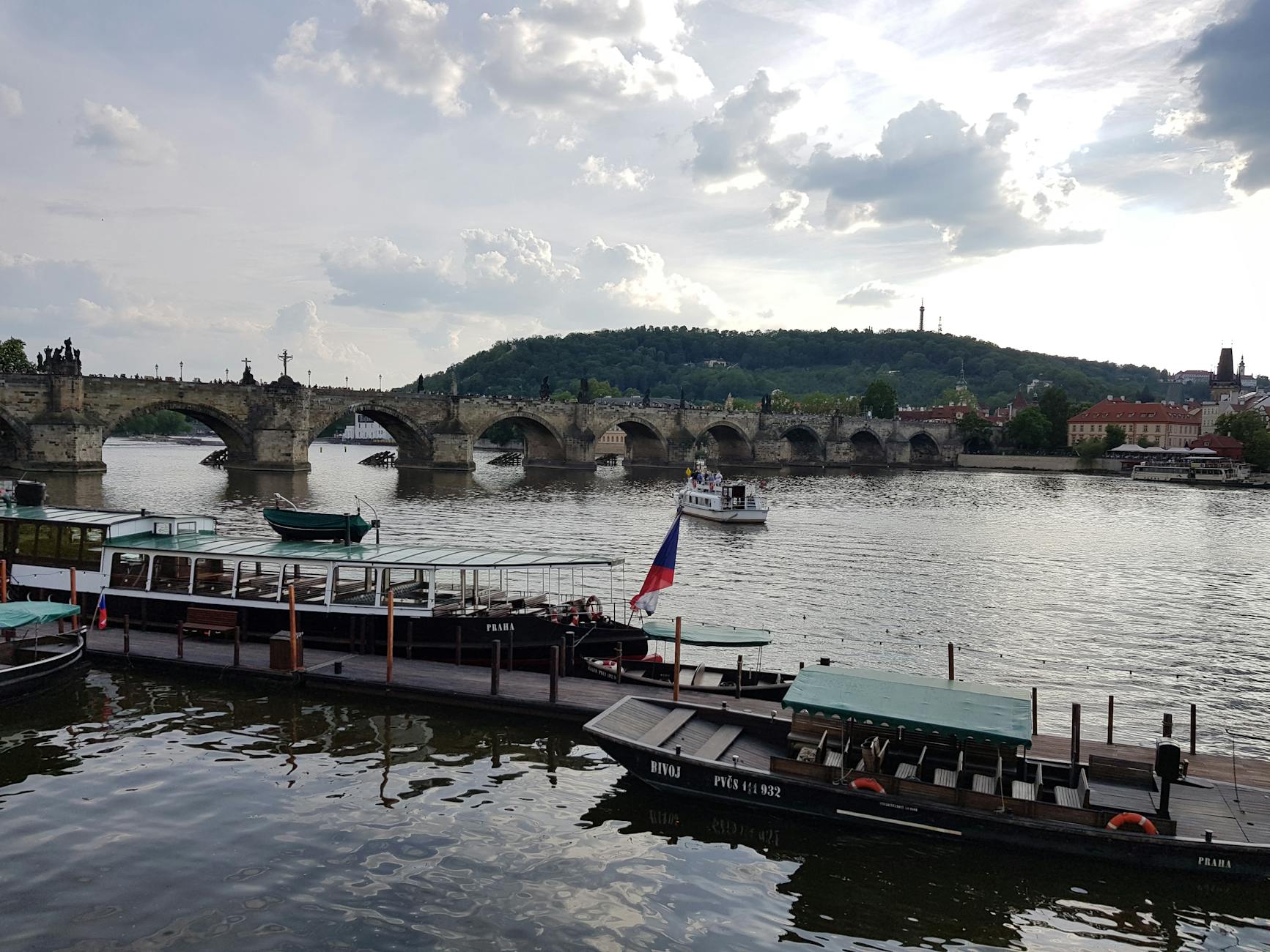 Charles Bridge with boats on the Vltava River under cloudy sky