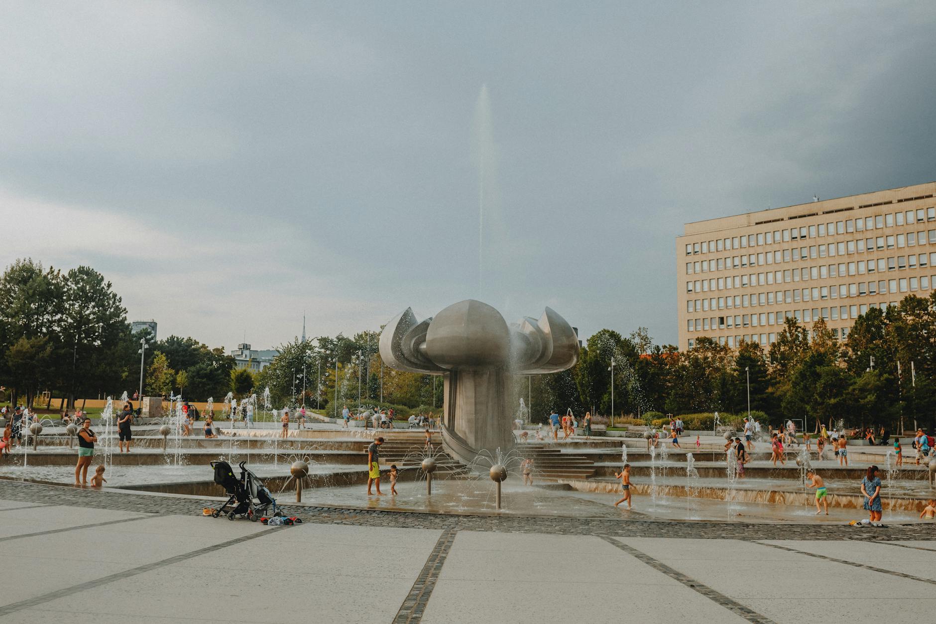 Families and children playing near a fountain in a Prague park