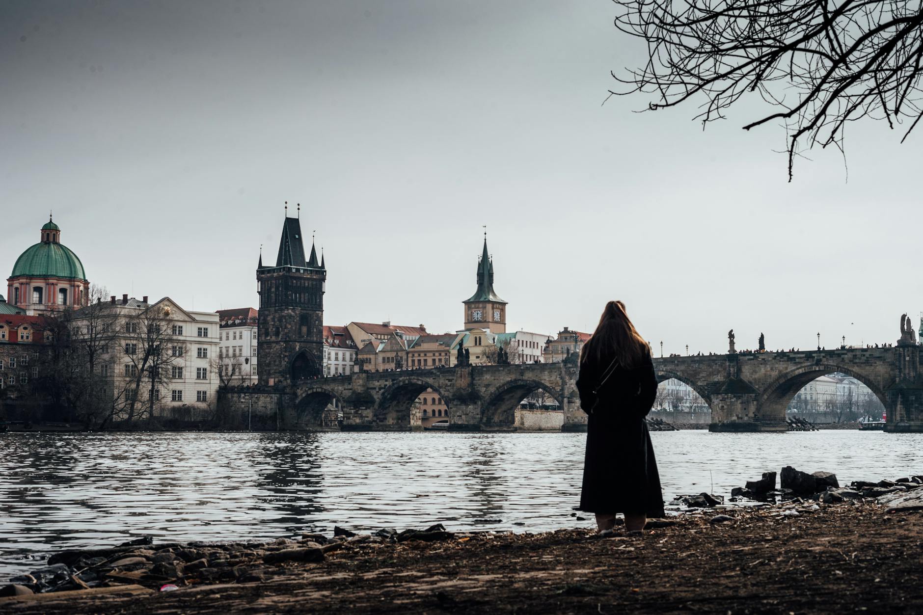Woman standing by the Vltava River overlooking Charles Bridge at dawn