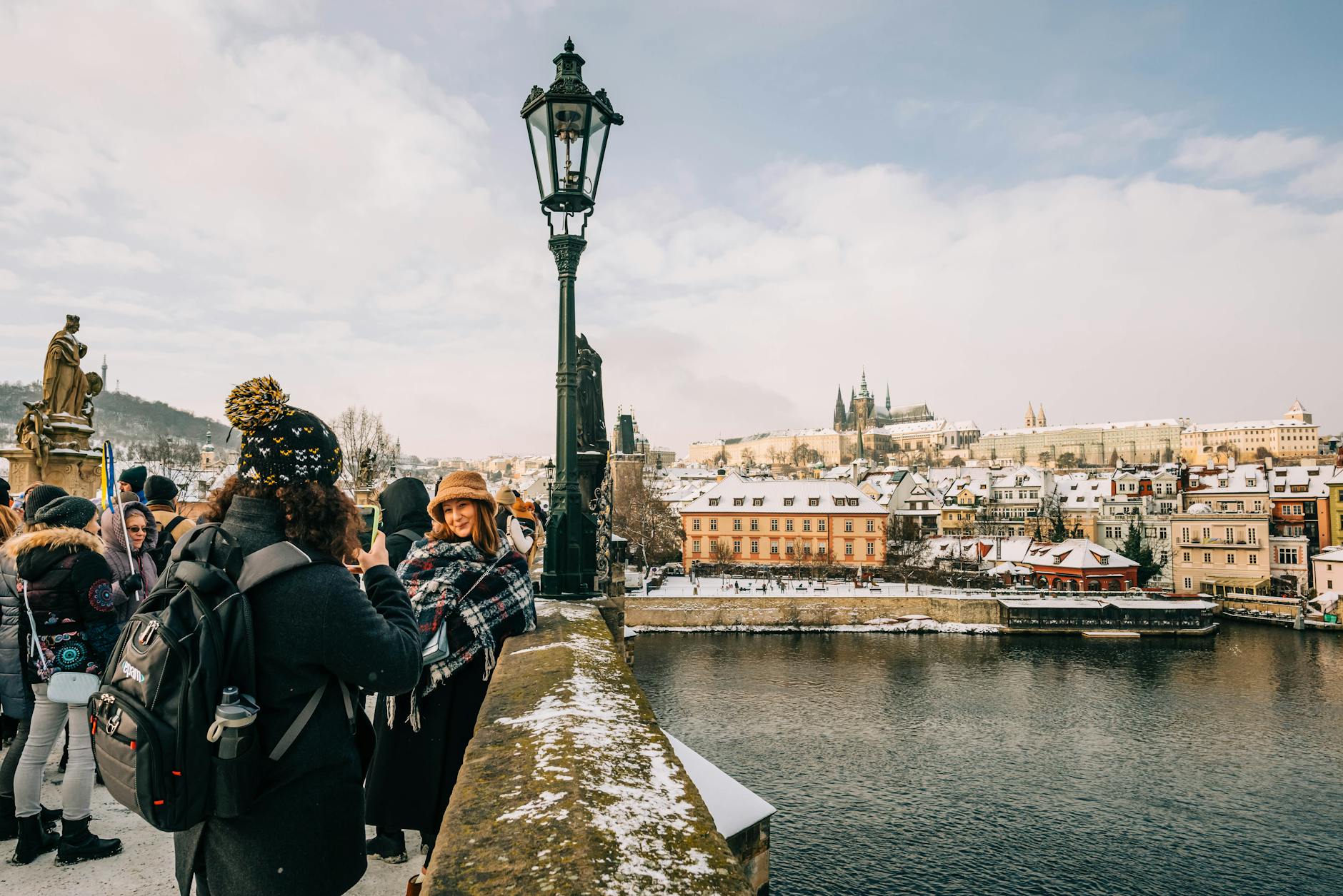 Travelers photographing Charles Bridge in winter with Prague Castle behind it