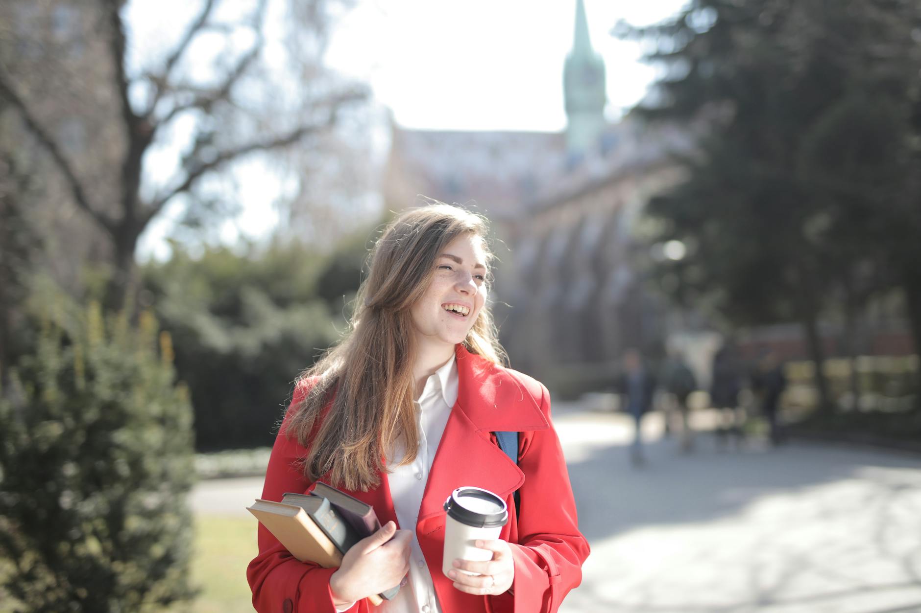 Student holding books and coffee on a university lawn