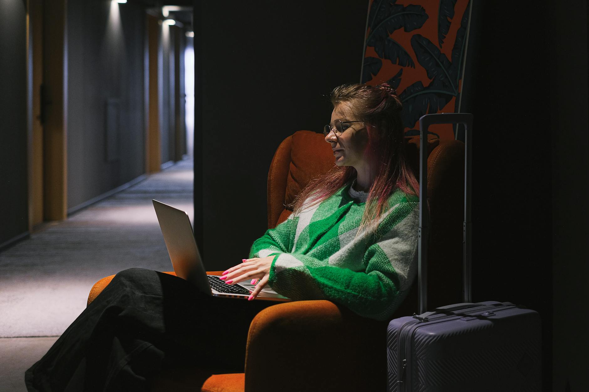 Woman working on a laptop in a hotel hallway beside luggage