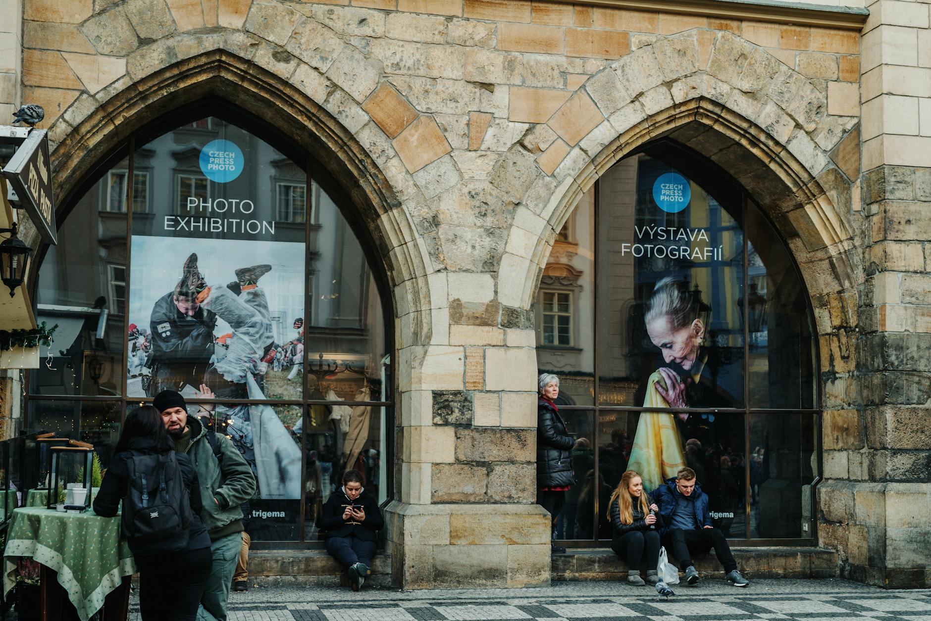 People walking past a photography exhibition entrance in Prague