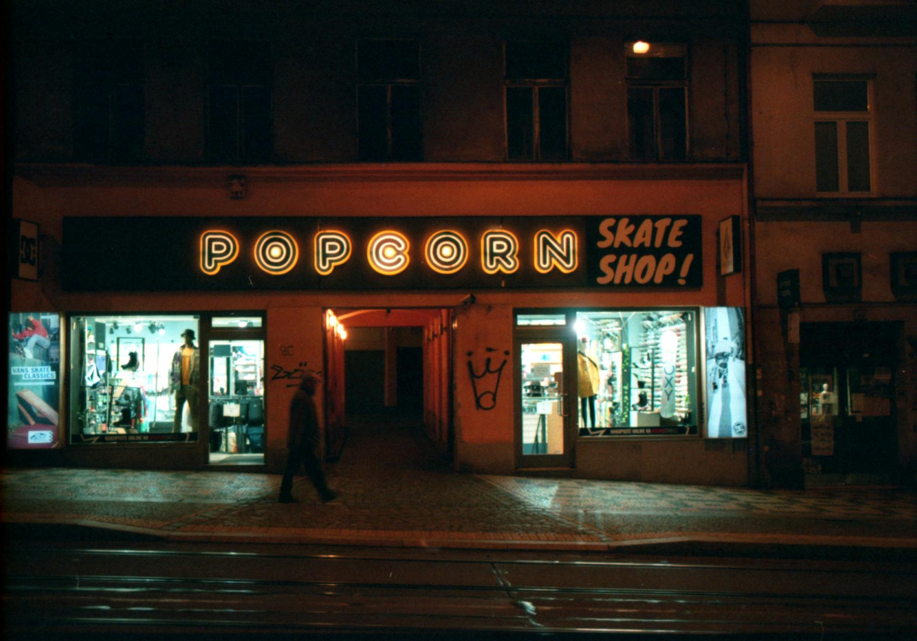 Person walking past a neon-lit shop in Prague at night