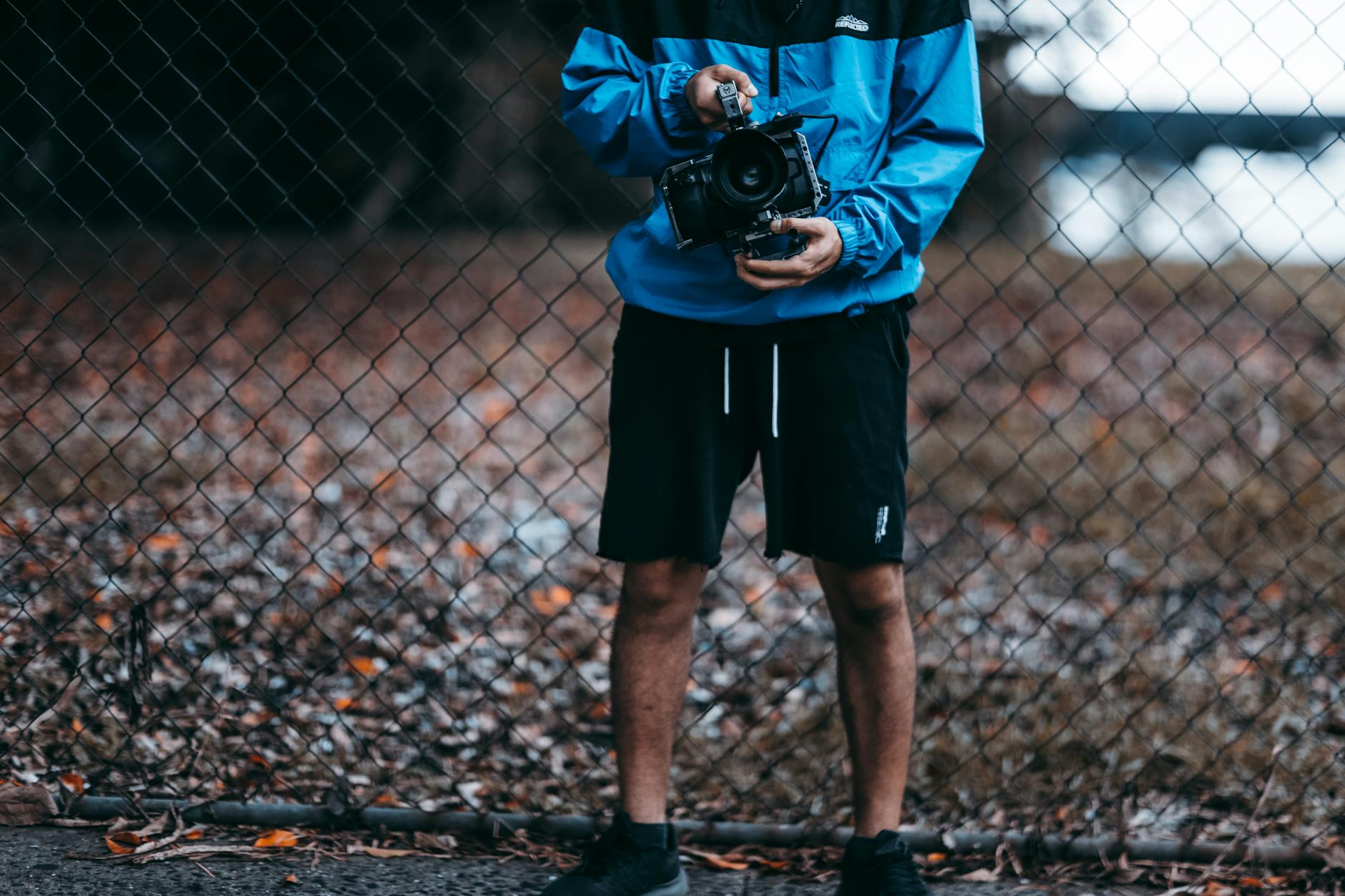 Person holding a camera outdoors by a fence