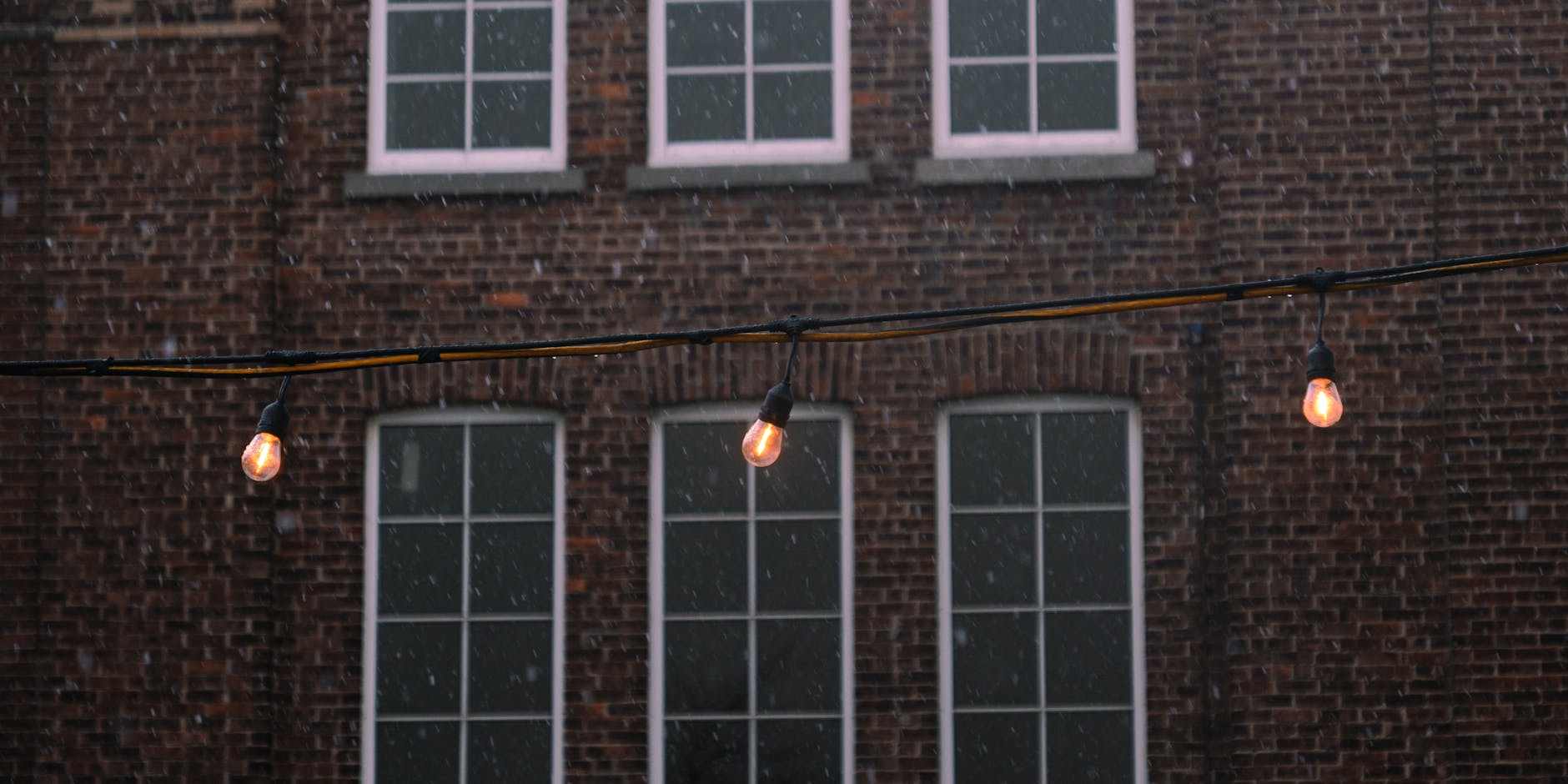 String lights hanging near a brick building during snowfall in Quebec