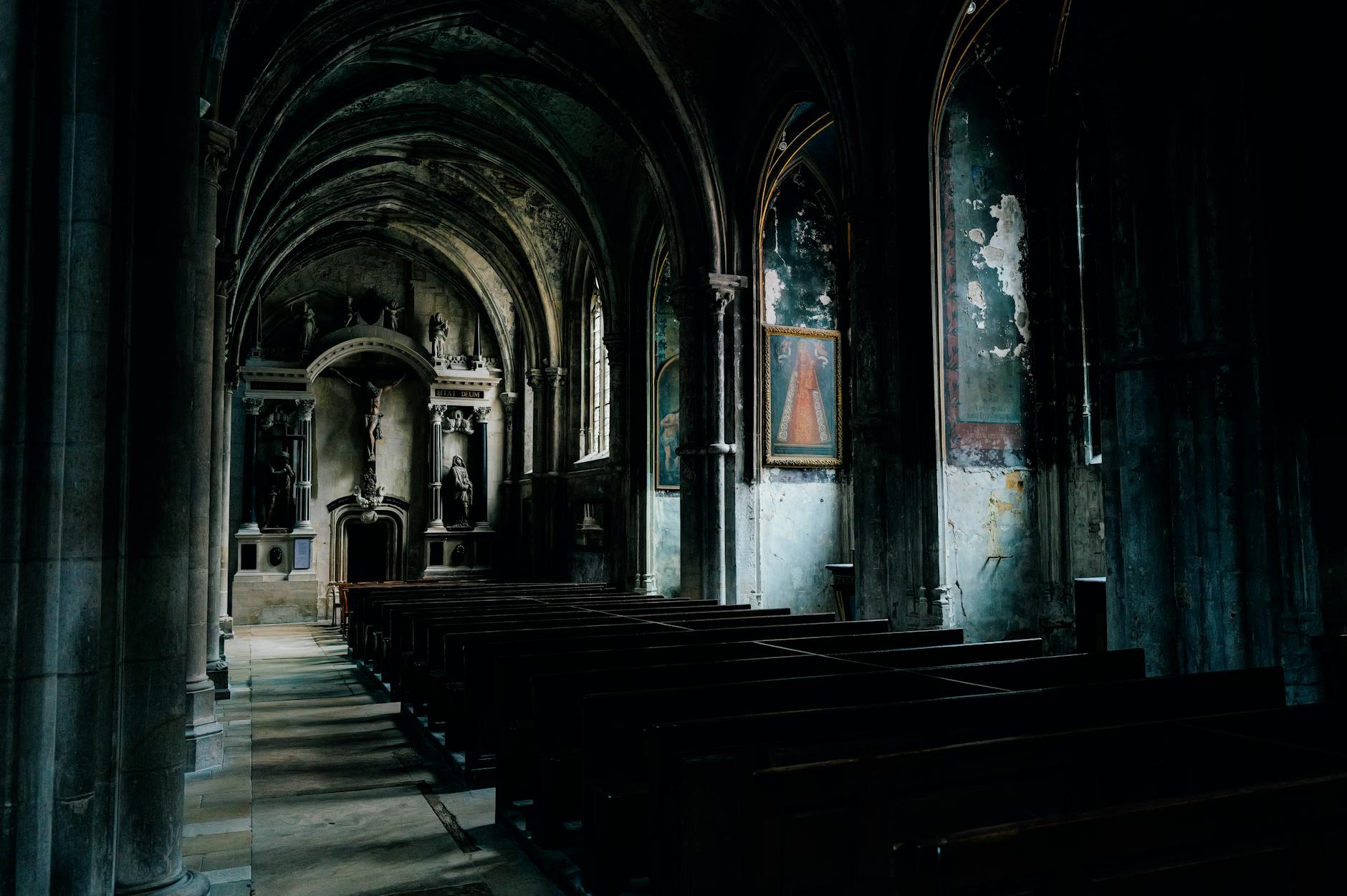 Dimly lit Gothic church interior with arches and religious artworks