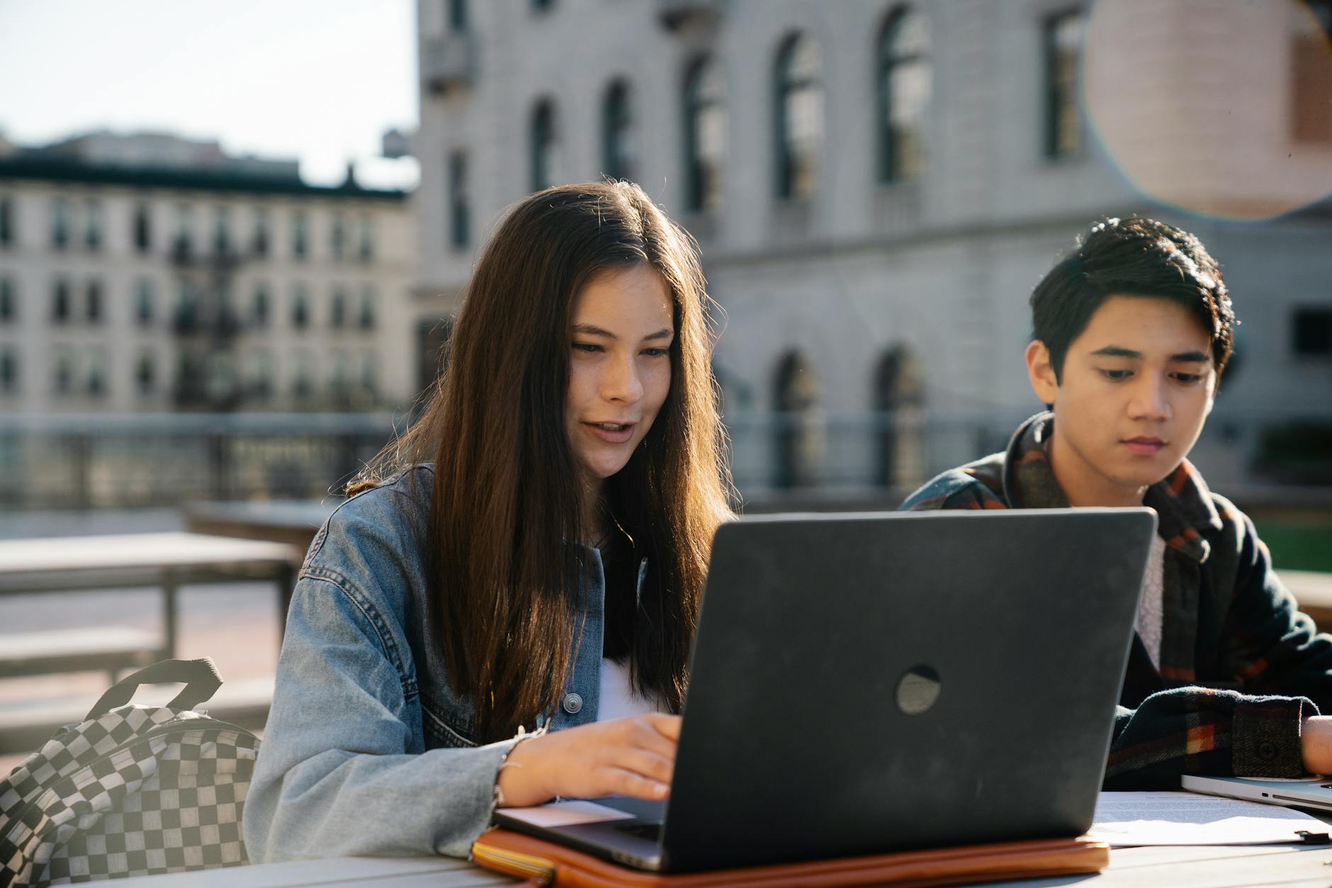 Two students collaborating on a laptop outdoors near a historic building