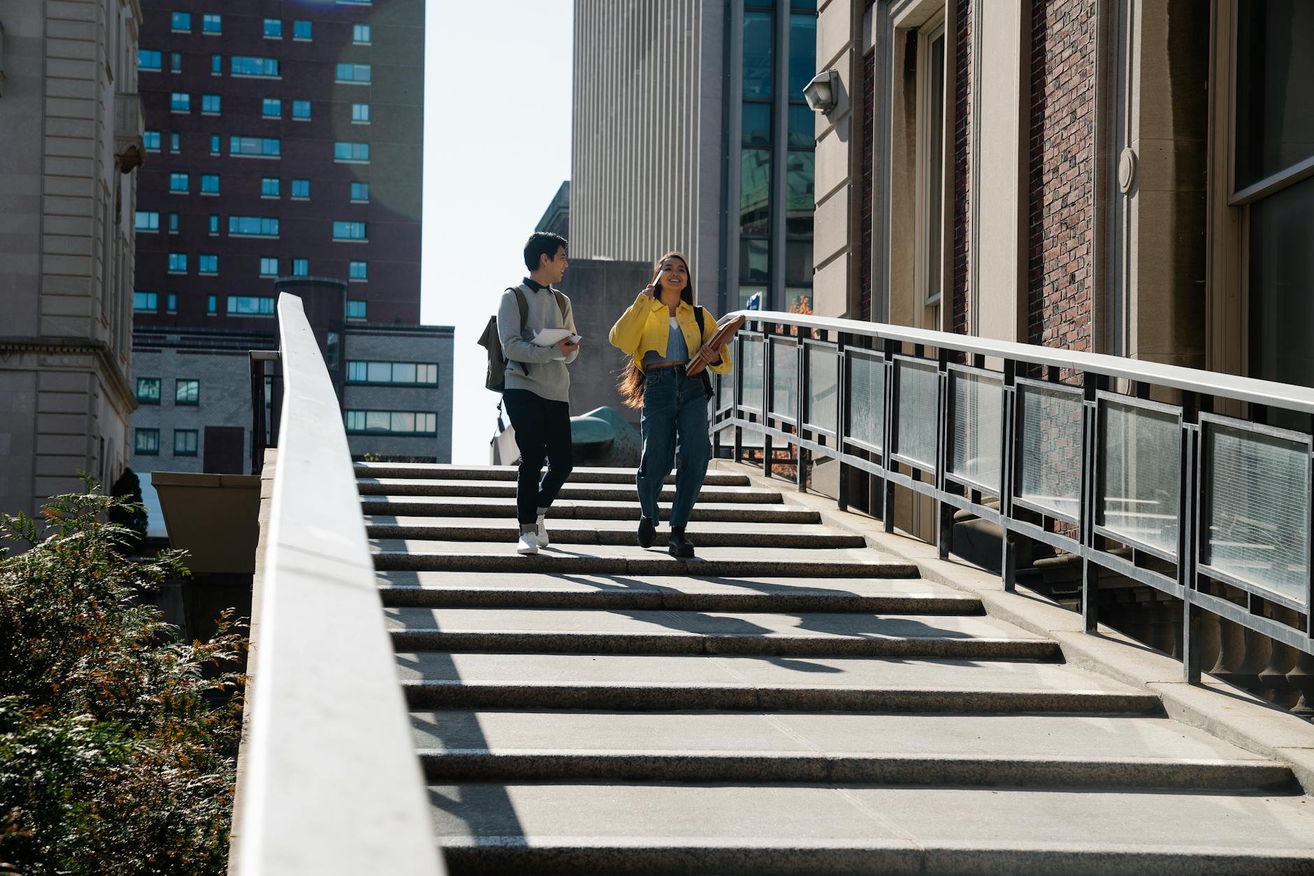Two students walking on campus stairs with papers