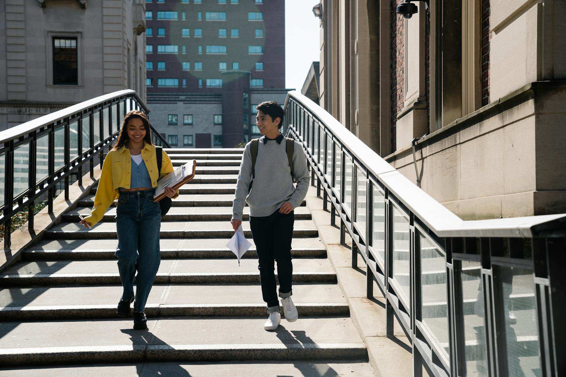 Two university students walking down stairs with documents