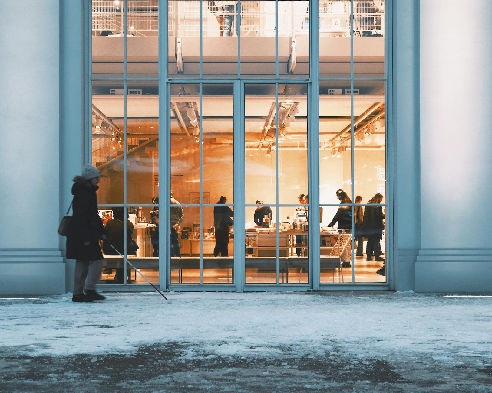 Woman with a white cane outside a lit building on a snowy day