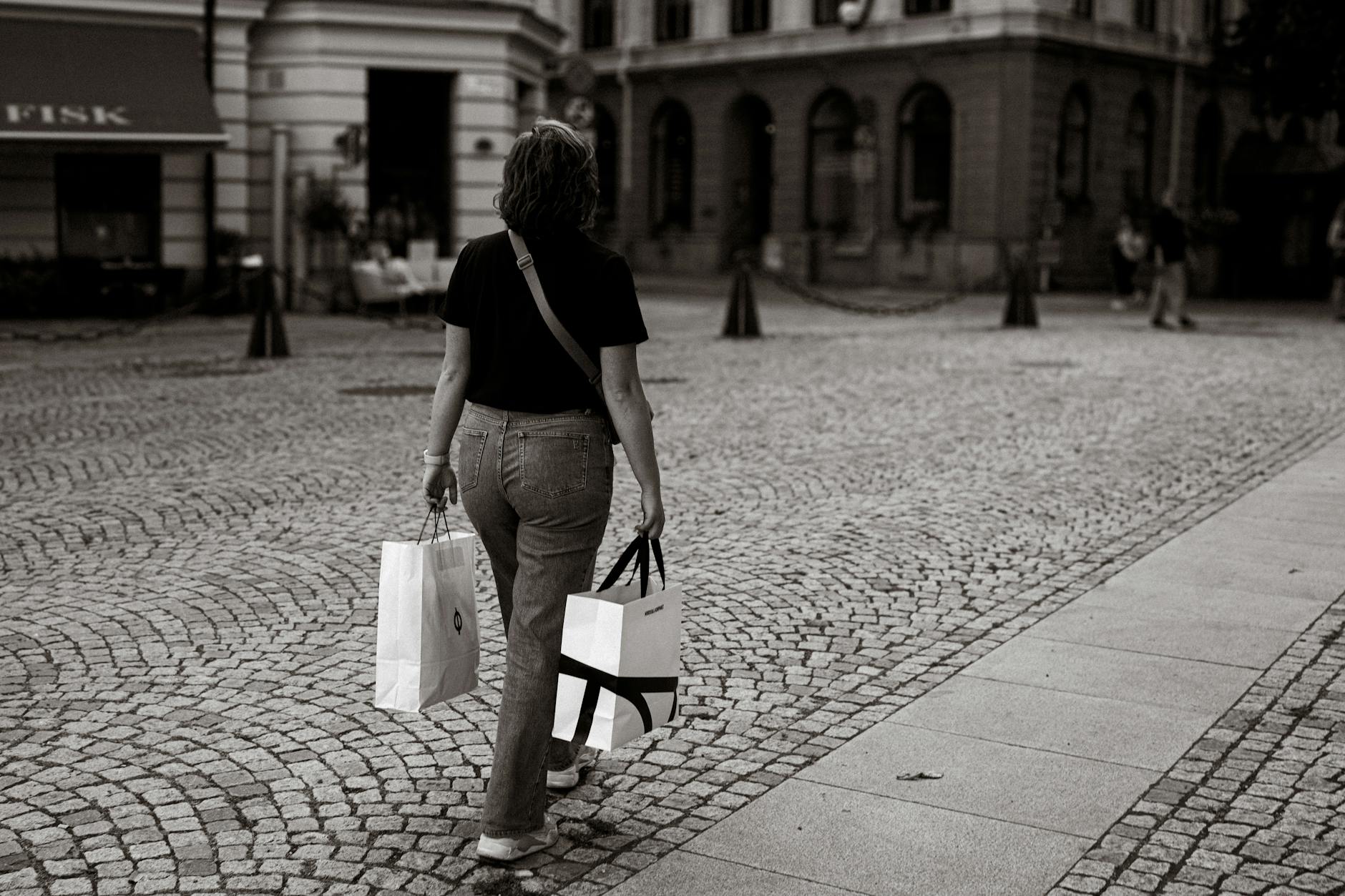 Woman with shopping bags on a Stockholm cobblestone street for luggage planning.