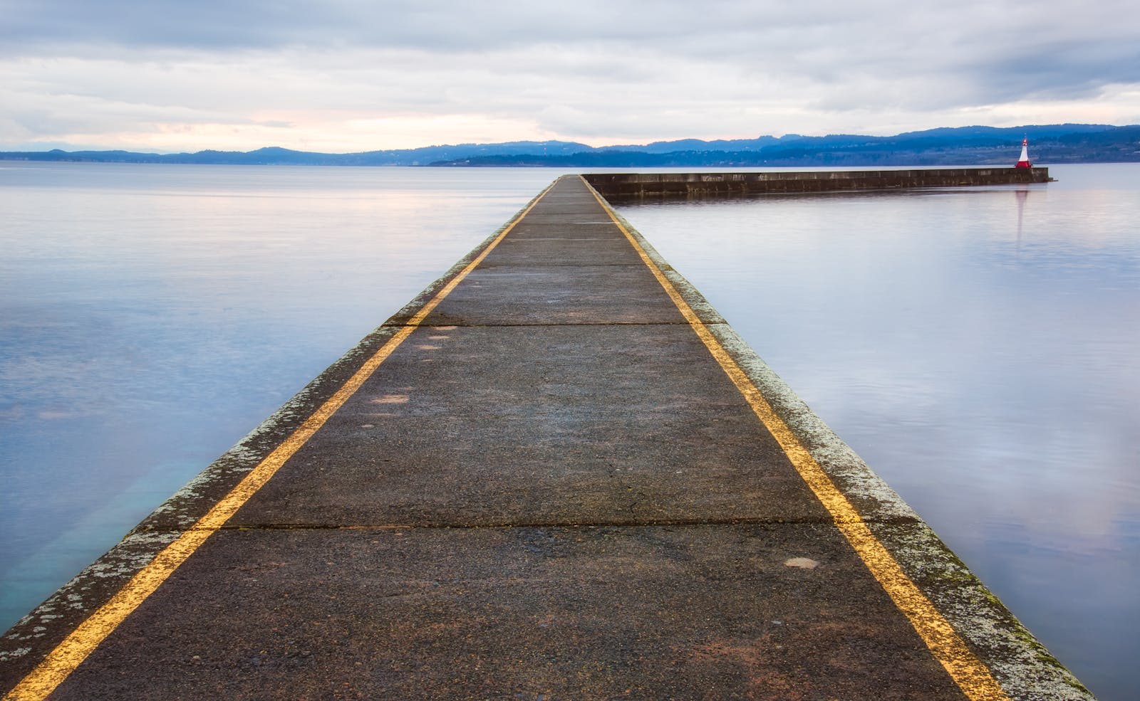 Pier leading to a lighthouse under a cloudy sky in Victoria, BC.