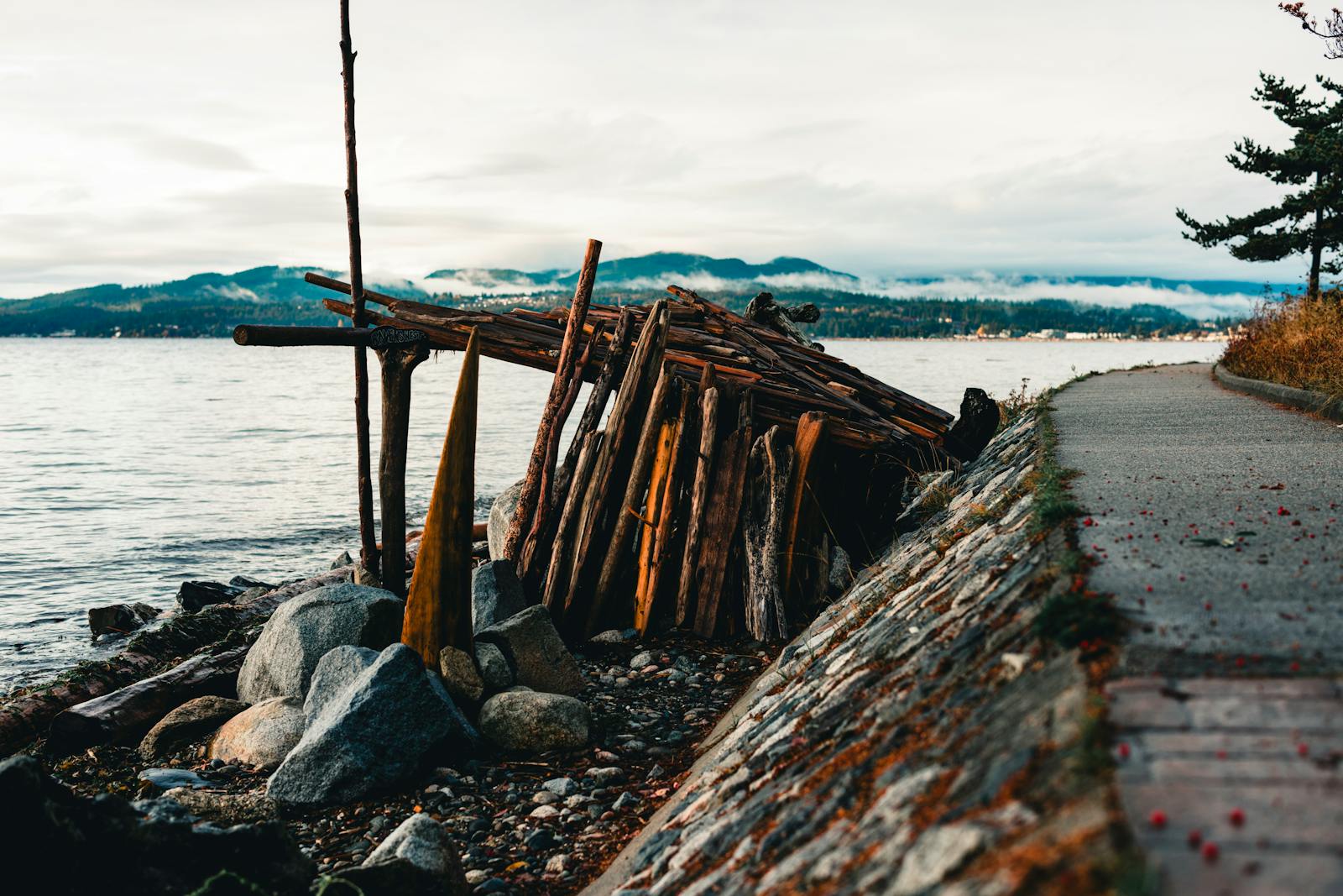 A rustic driftwood structure on a pebble beach by a path in Gibsons, BC.