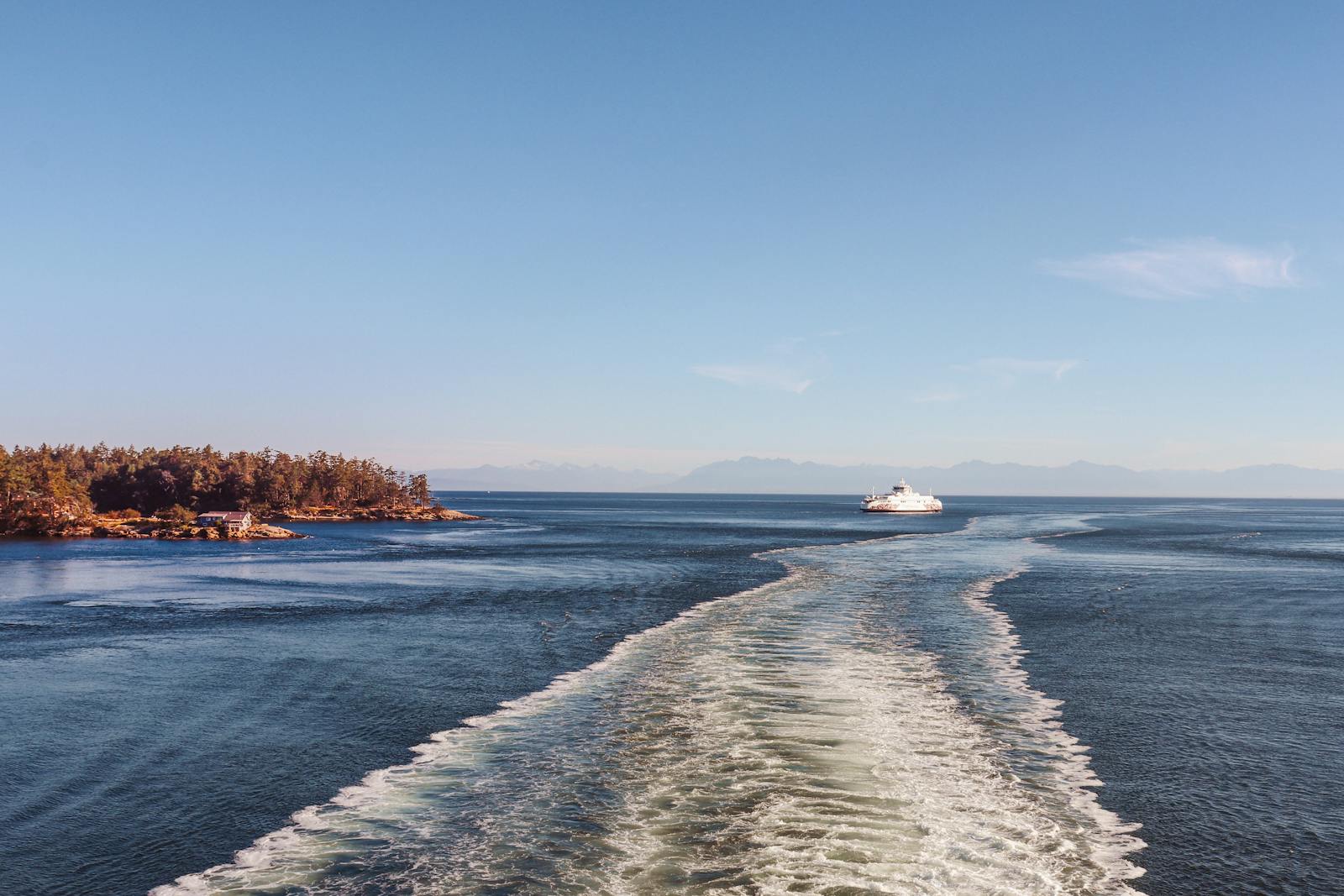 A ferry moves across calm sea near a wooded island under a clear blue sky.