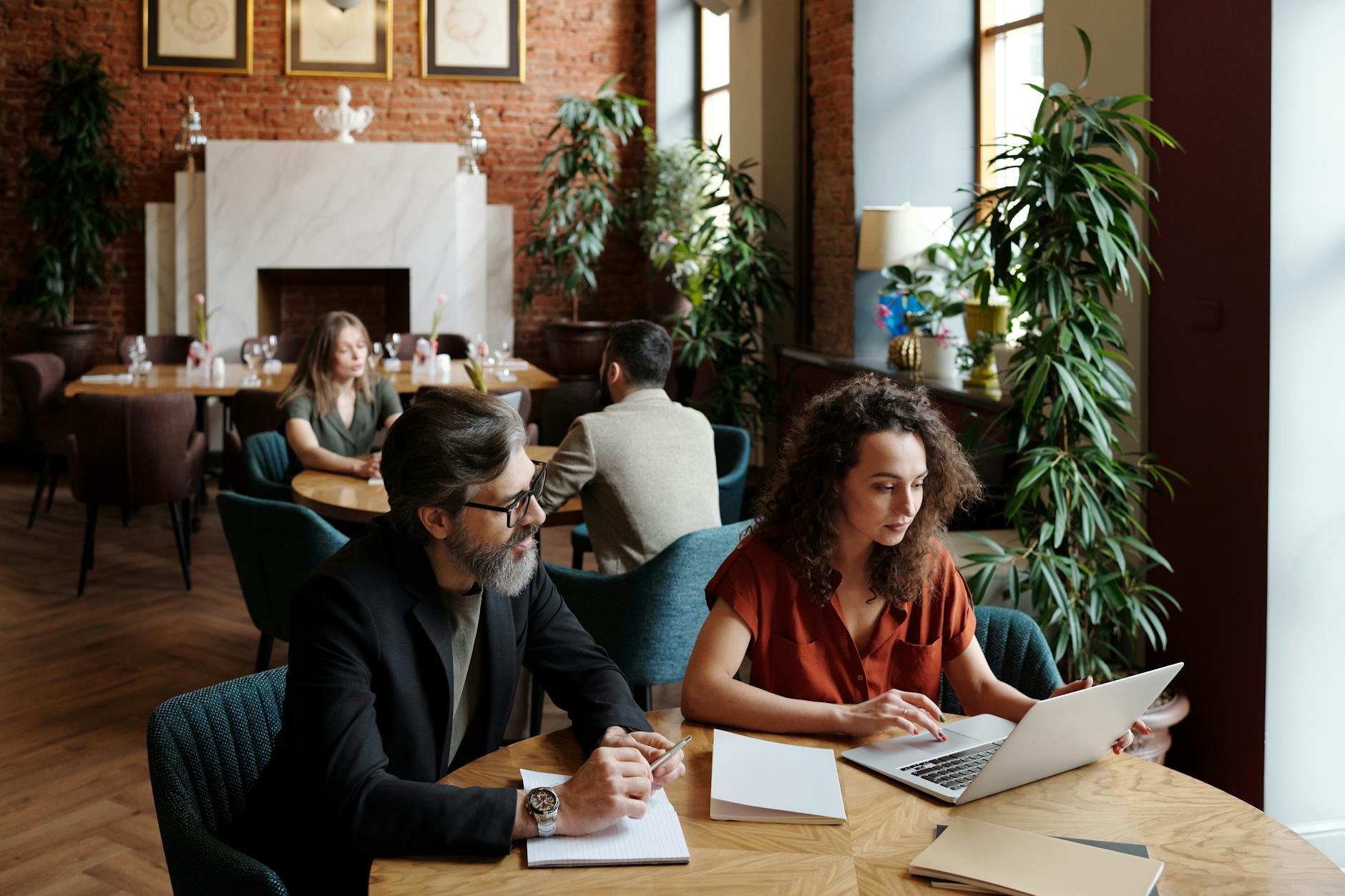 Team discussing plans over laptops and notes in a stylish coffee shop setting.