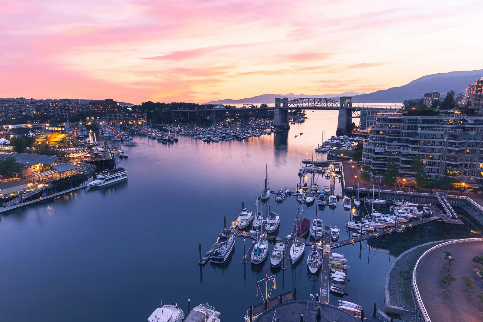 Sweeping view of Vancouver harbor and skyline at twilight, featuring boats and Burrard Bridge.
