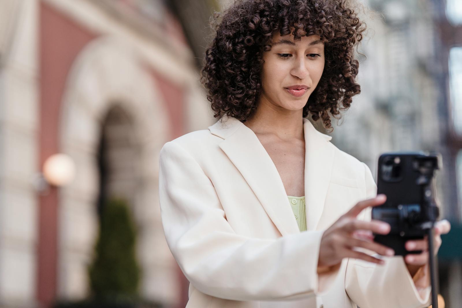Young vlogger with curly hair preparing cellphone for video recording in town.