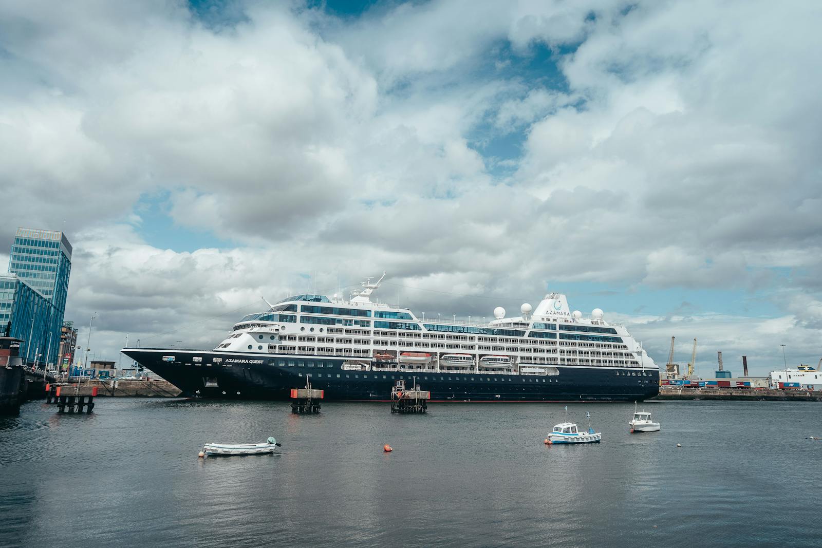 Large cruise ship docked in a harbor with smaller boats and cloudy skies.