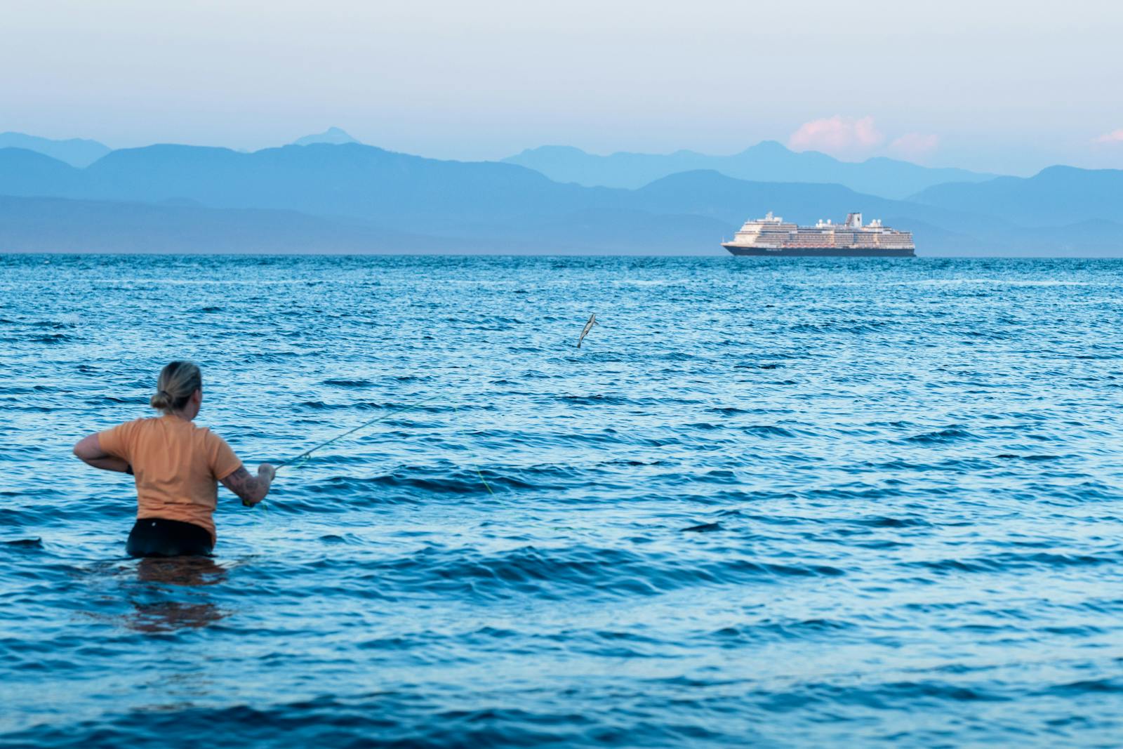Person fishing on the ocean near Campbell River, BC with a cruise ship in the background.
