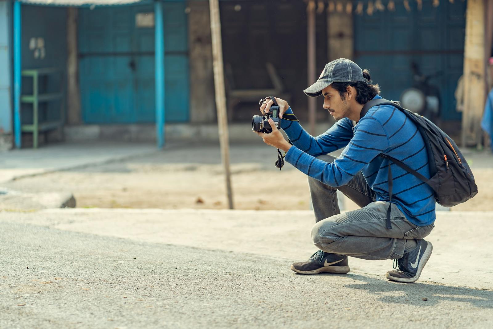 A young man crouching to take photos with his DSLR camera in an urban environment.