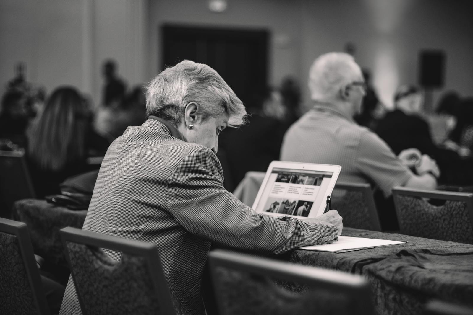 A senior journalist takes notes during a conference, engrossed in thought.