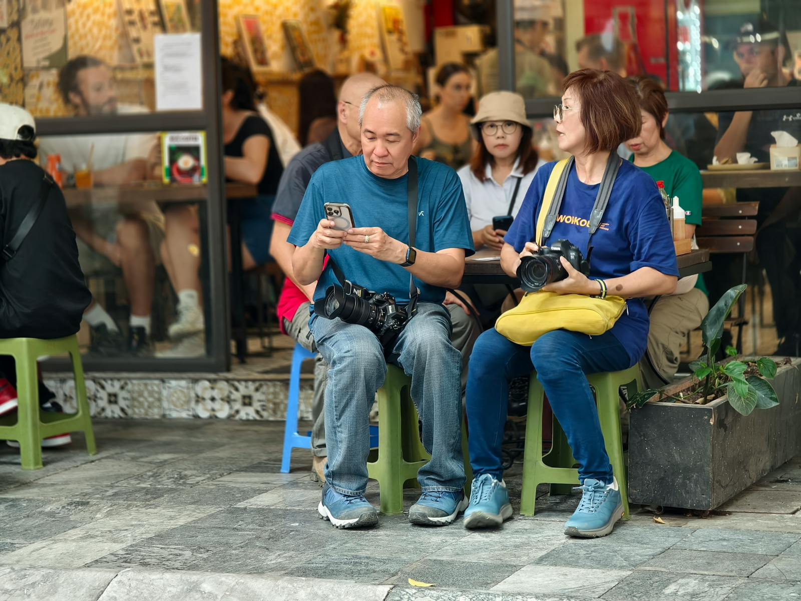 Photographers sitting at an outdoor cafe, capturing moments and interacting with devices.