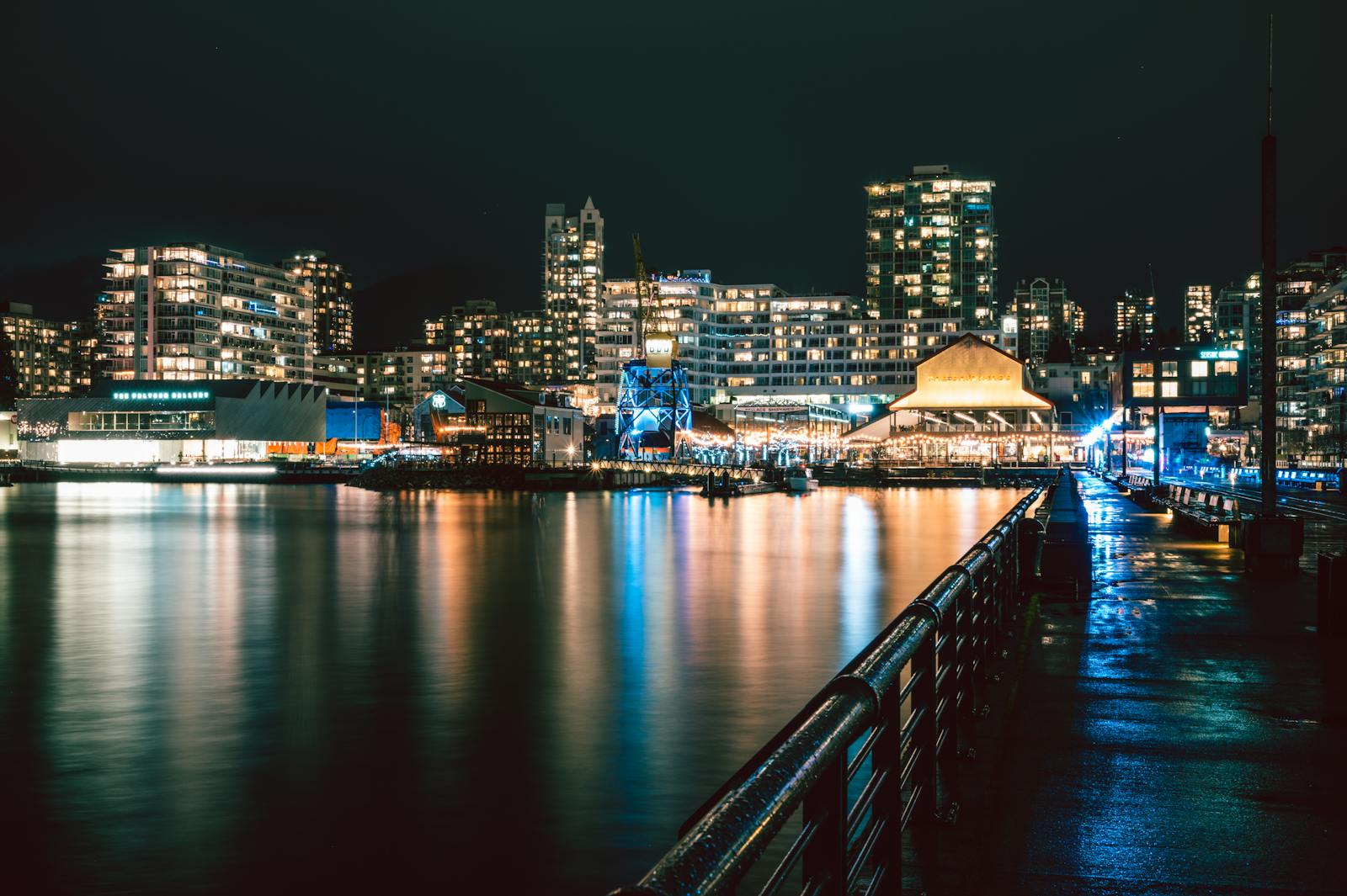 Illuminated waterfront skyline in North Vancouver at night with city lights reflected on water.
