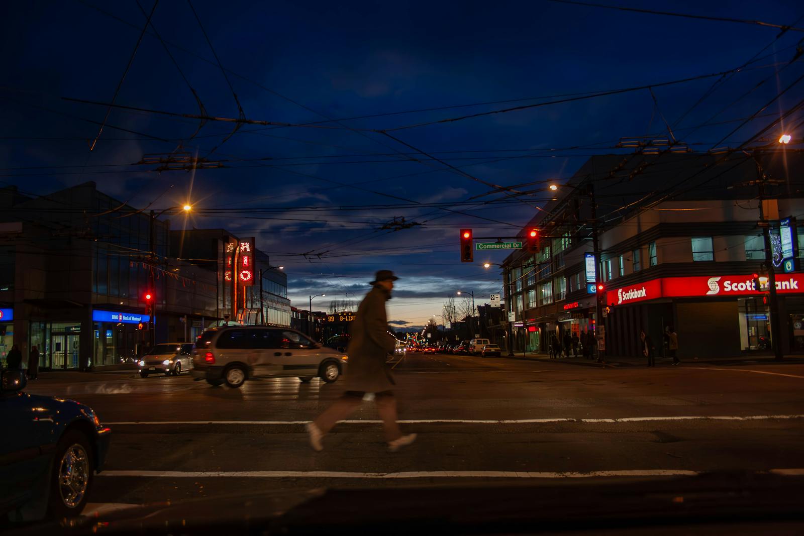 Dynamic night scene of a Vancouver intersection with pedestrians, cars, and bright city lights.