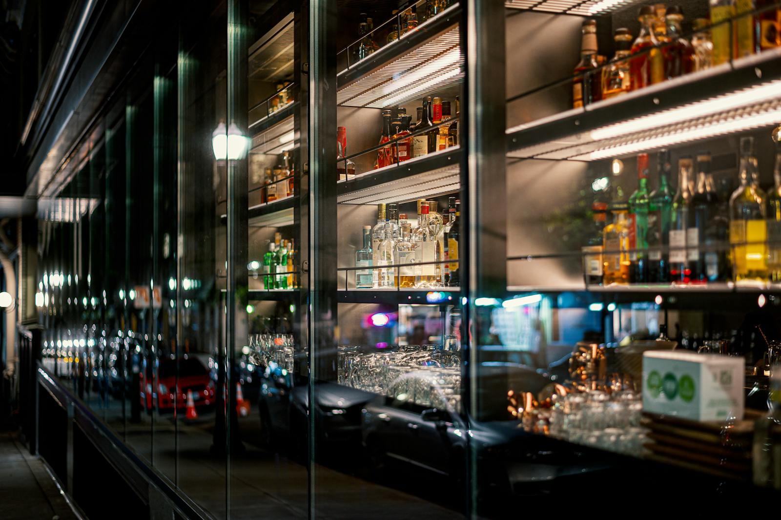 Bar shelves with liquor bottles and reflections of street lights at night.