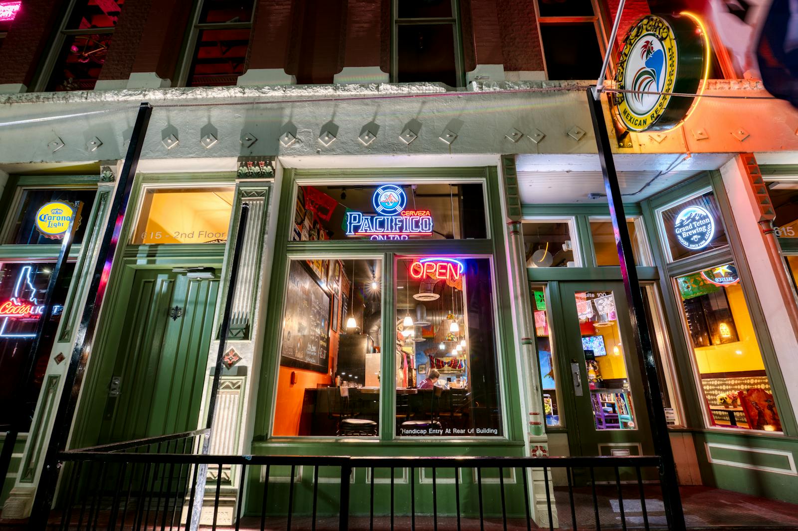Illuminated modern cafe exterior with green doors and neon signs on a city street at night.