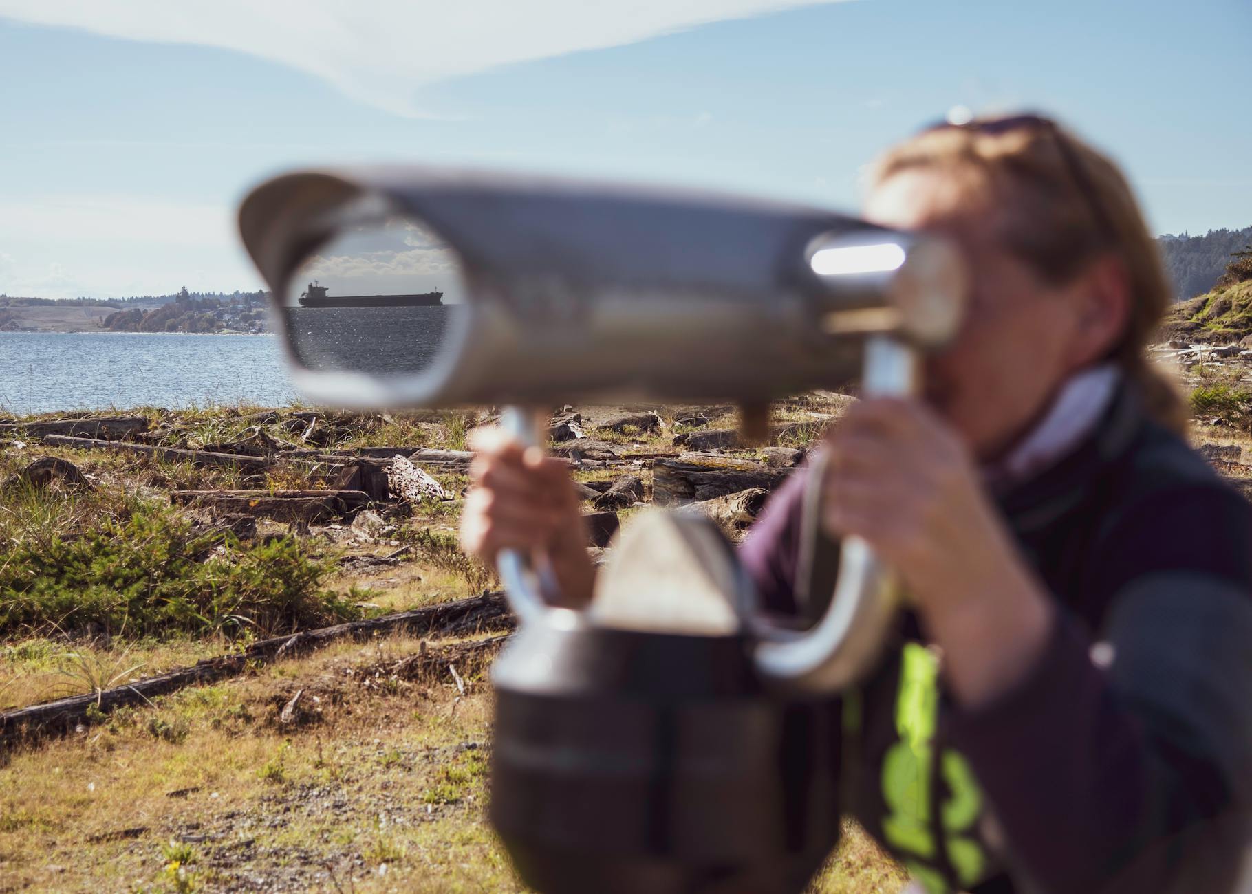 Woman using binoculars to view a distant ship along the Colwood shore