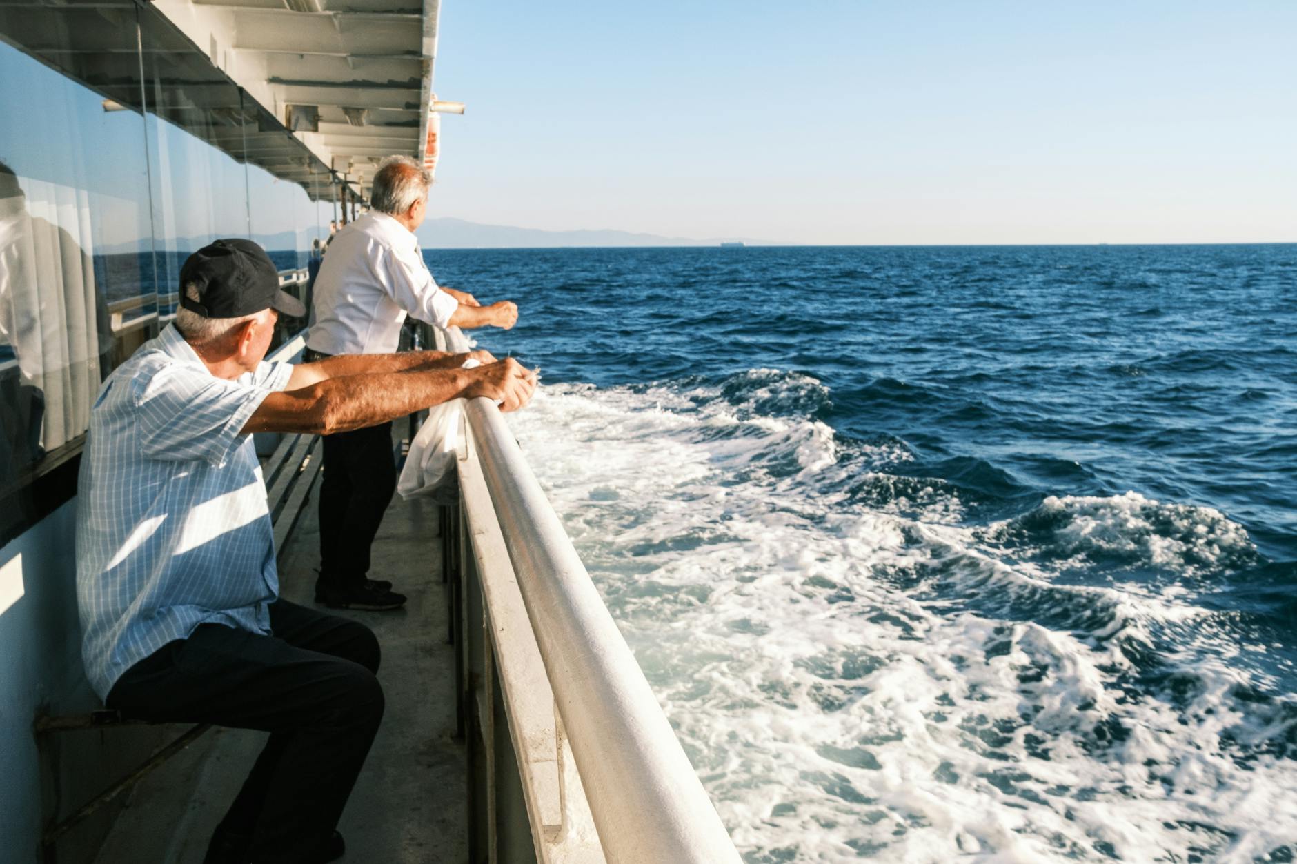 Two senior men looking out from a ferry deck on a sunny day