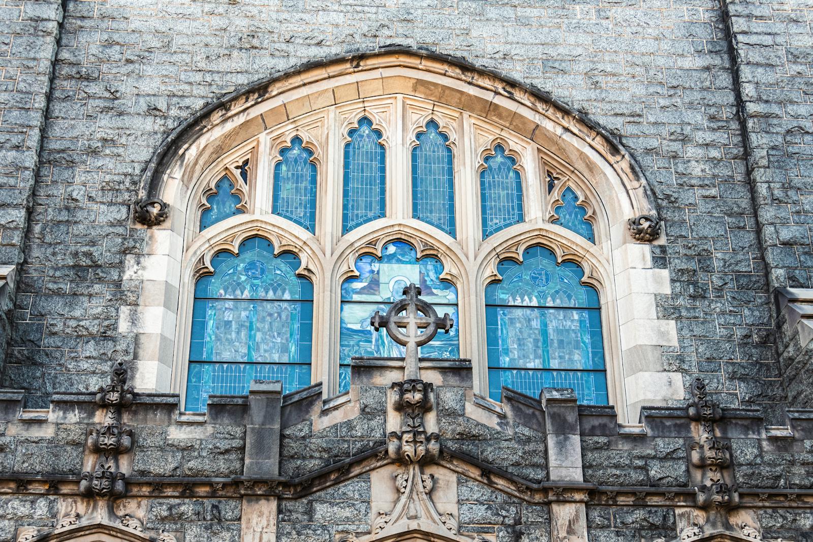 Beautiful Gothic church window with intricate stained glass and cross.