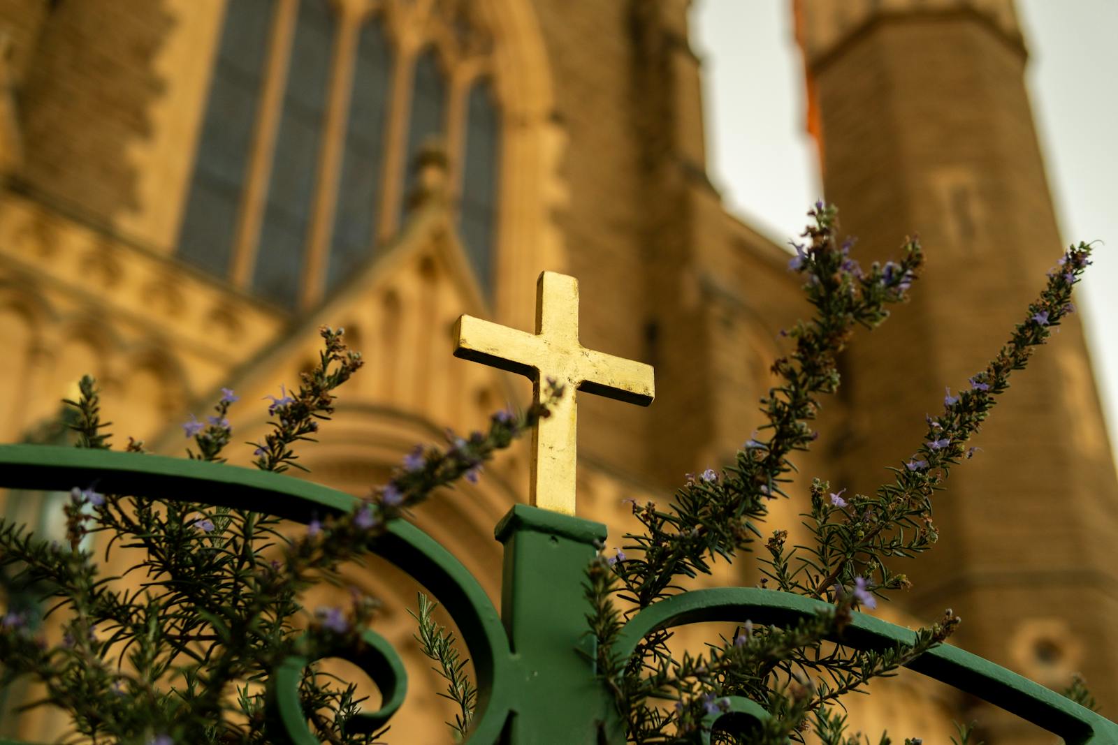 Gold cross set against a Gothic church backdrop with flowers in the foreground.