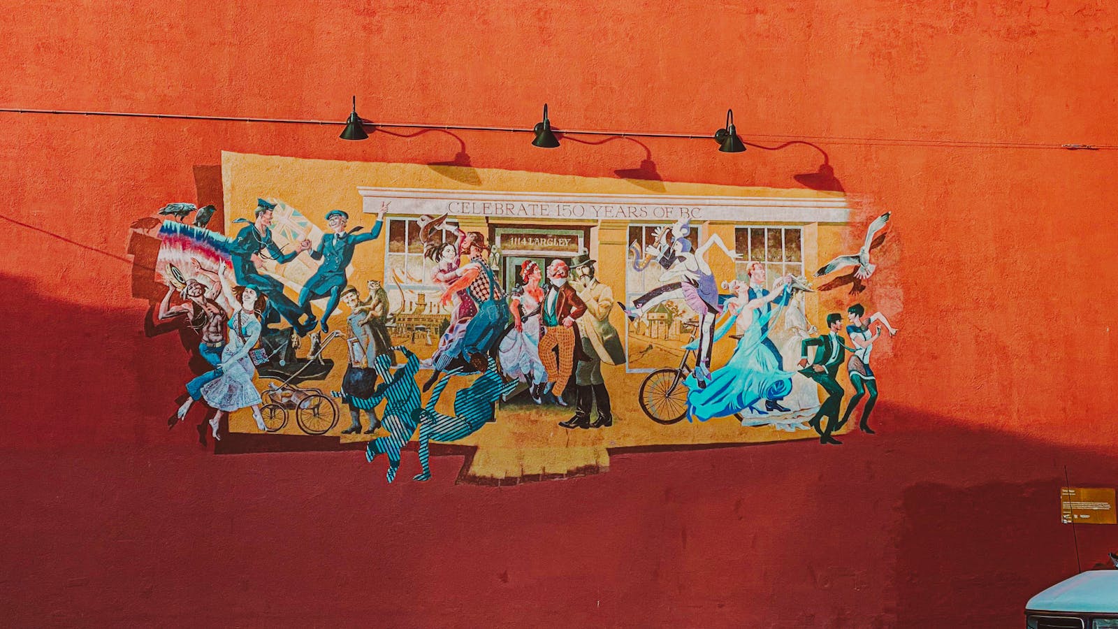 Street mural in Victoria, BC, depicting historical celebration and art on a red wall.