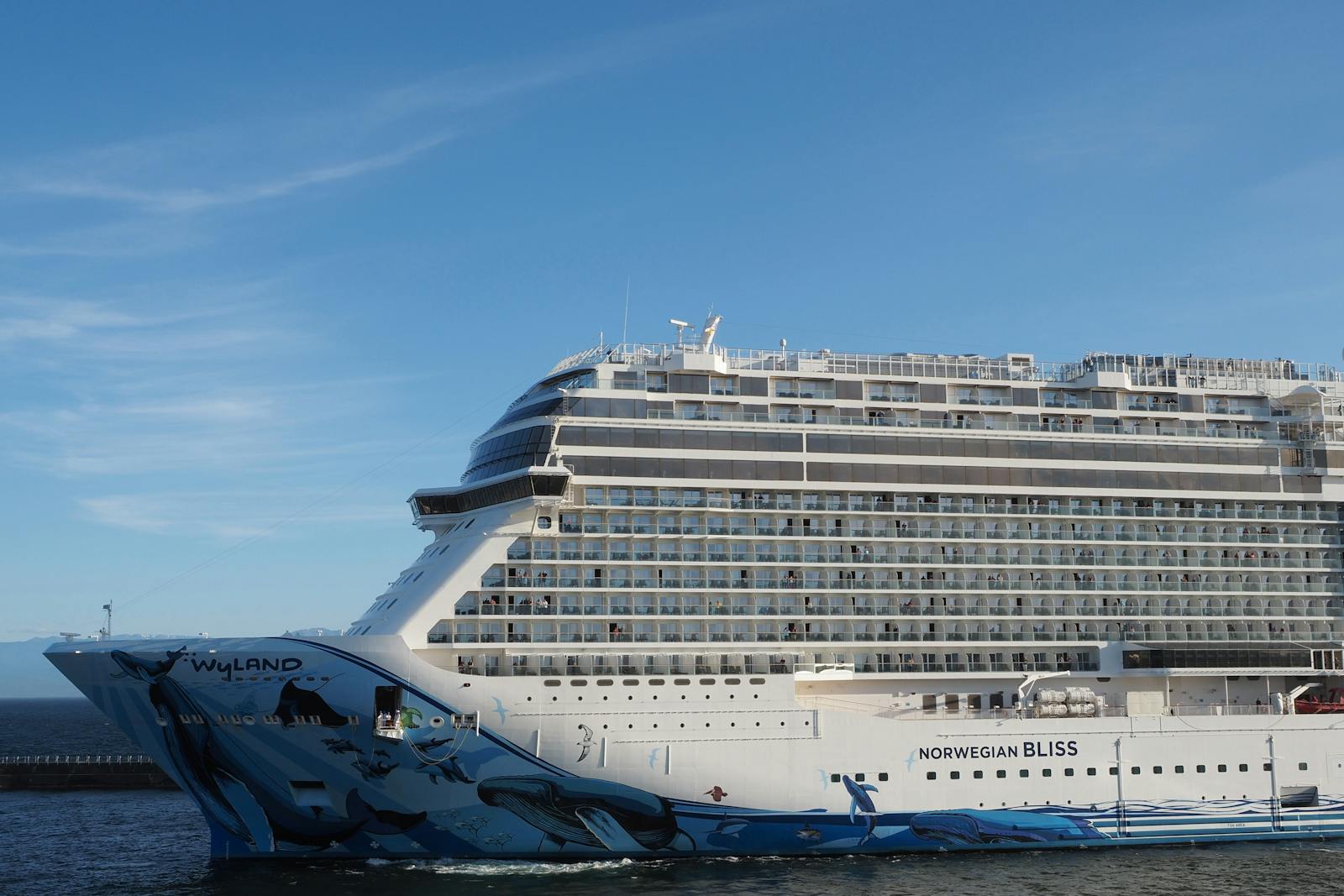A stunning side view of the Norwegian Bliss cruise ship docked in Victoria, BC, under a clear blue sky.