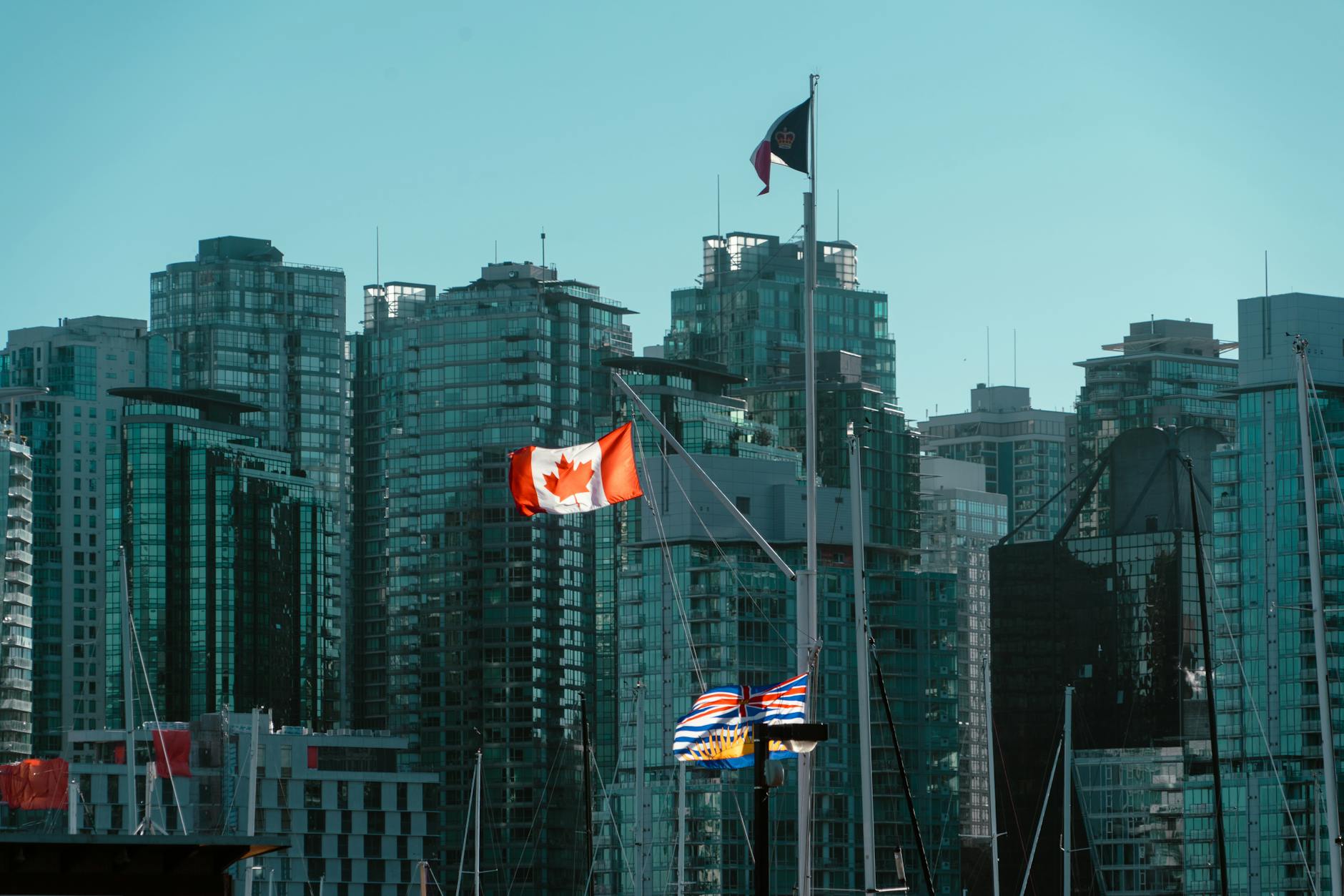 A view of Vancouver's glassy skyscrapers with Canadian and British Columbia flags waving in the foreground.