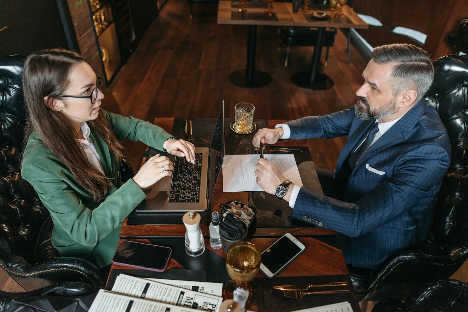 A businessman and businesswoman discuss documents over drinks in a stylish restaurant.